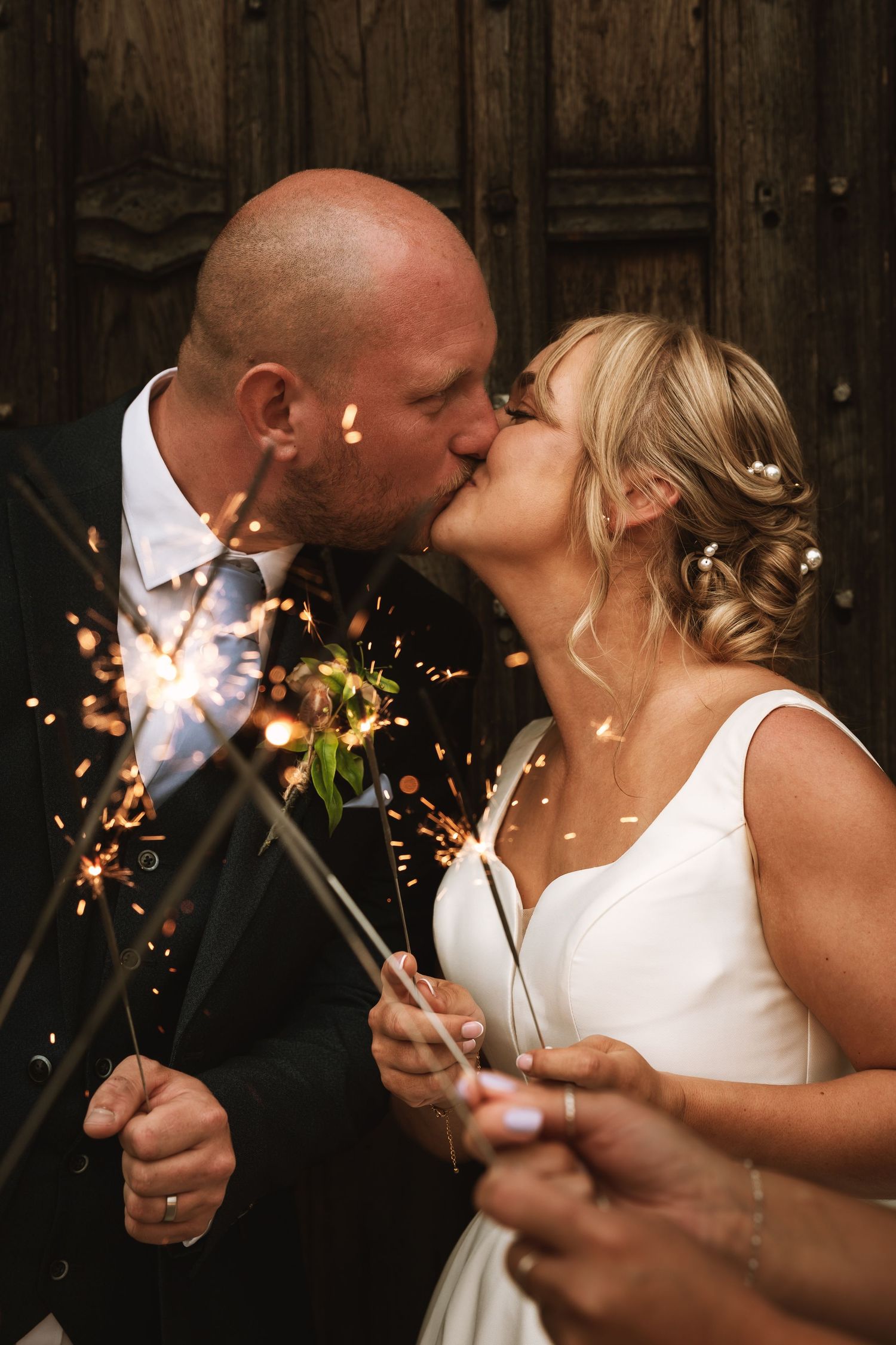 Newlyweds share romantic moments while holding sparklers in a rustic barn setting.