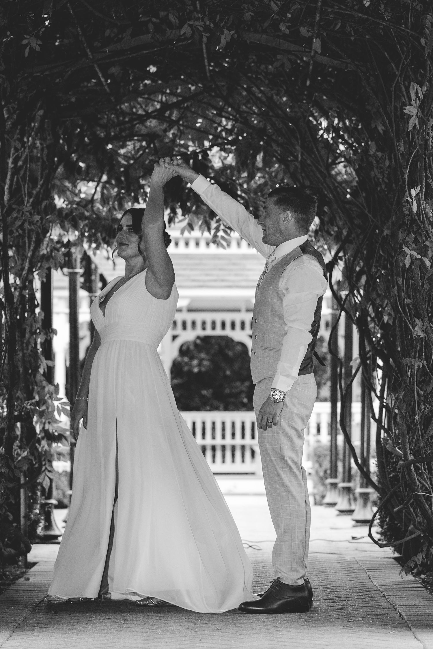 Wedding party walking under an archway of trees in white attire.