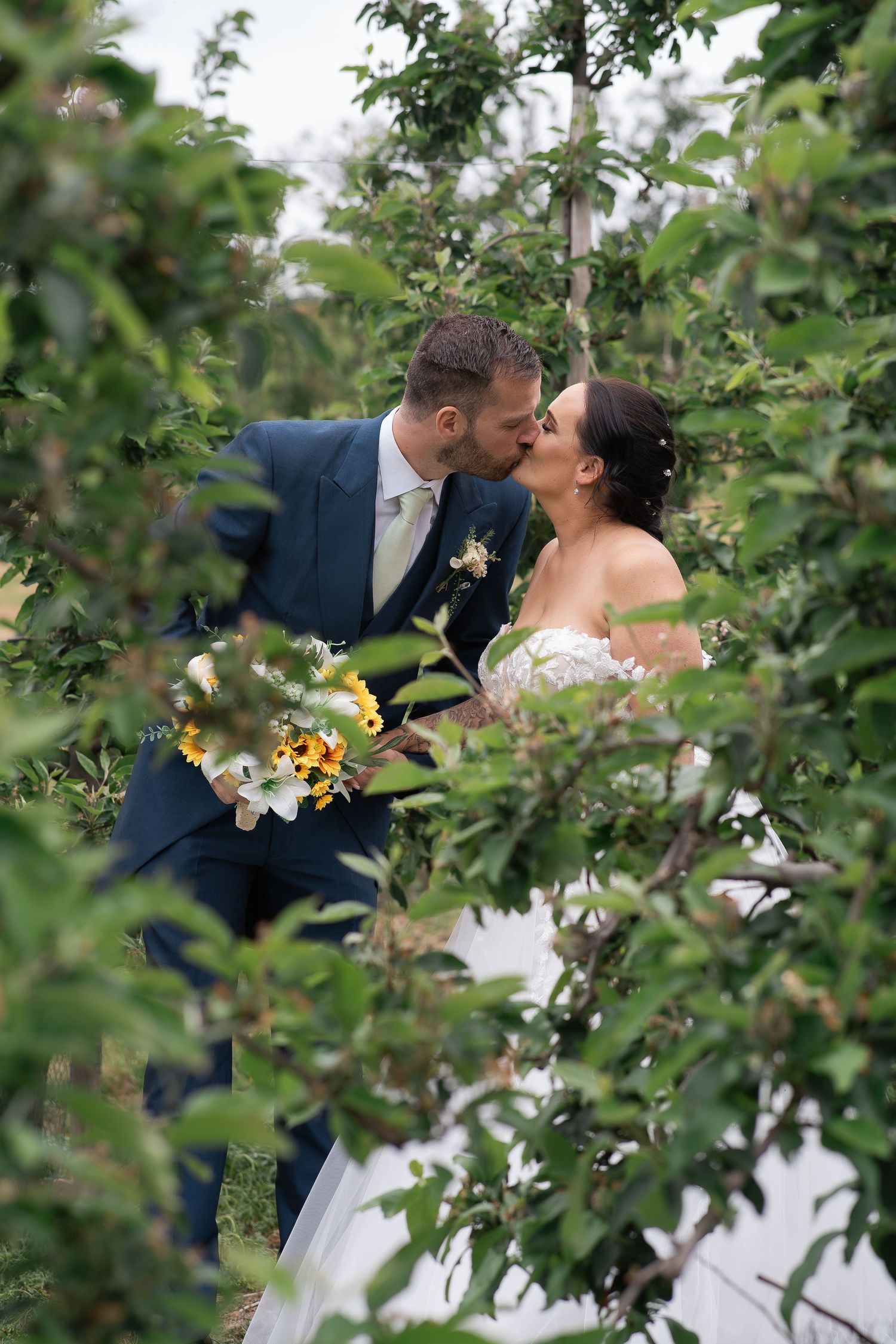 Romantic moment captured through green garden foliage with sunflowers in bouquet.