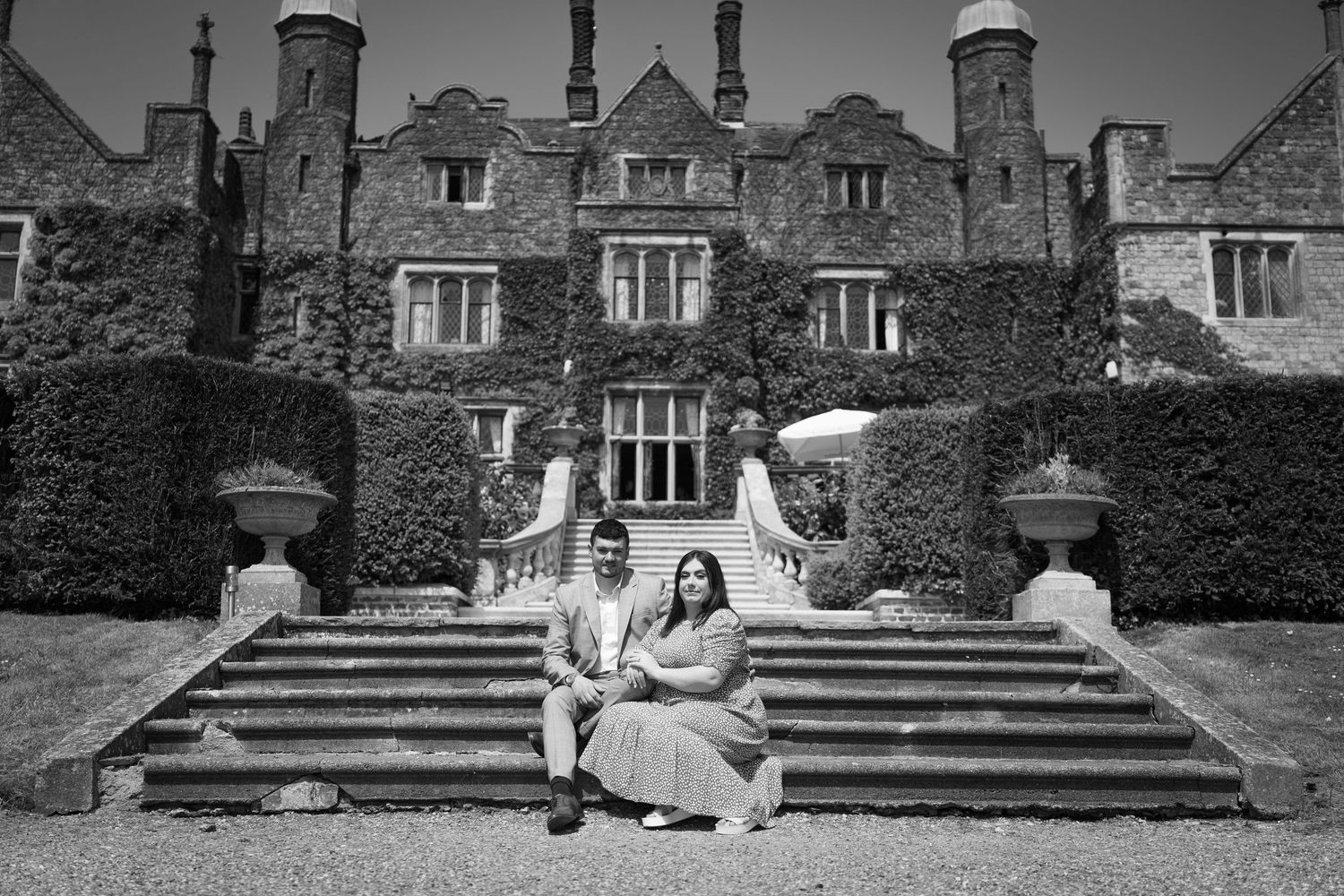 A couple poses on stone steps in front of a grand historic mansion building.