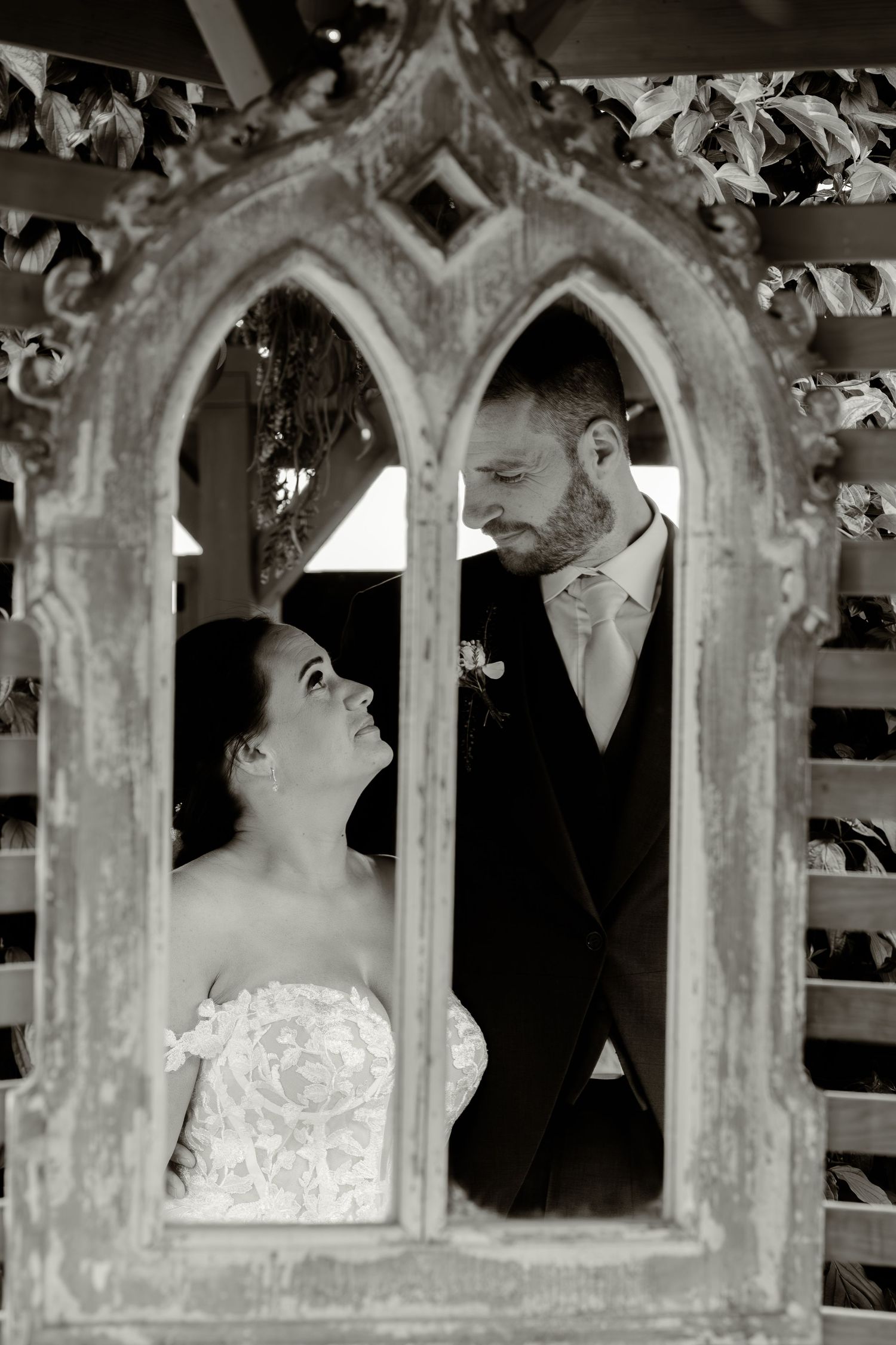 Romantic wedding couple shares intimate moments through gothic stone archways in black and white.