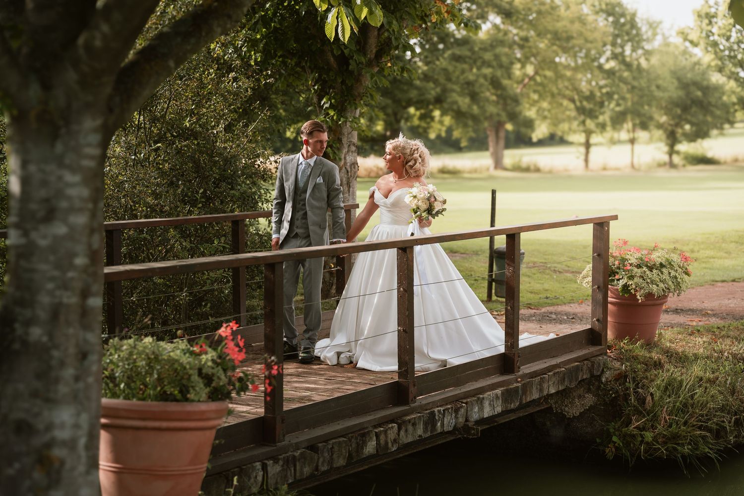 Wedding couple posing on rustic wooden bridge with floral decorations.