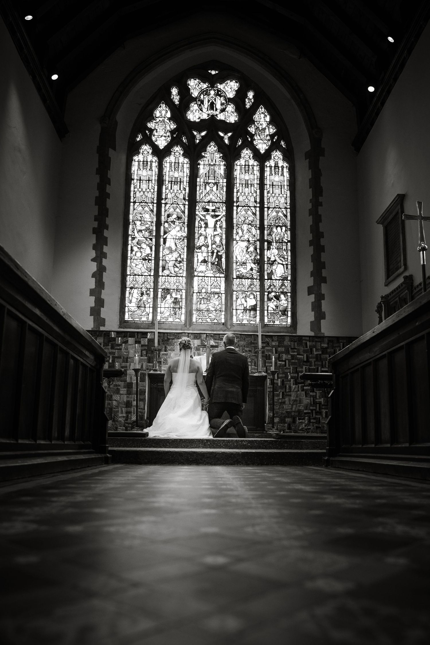 Dramatic black and white photo of church interior with ornate stained glass windows and pews.