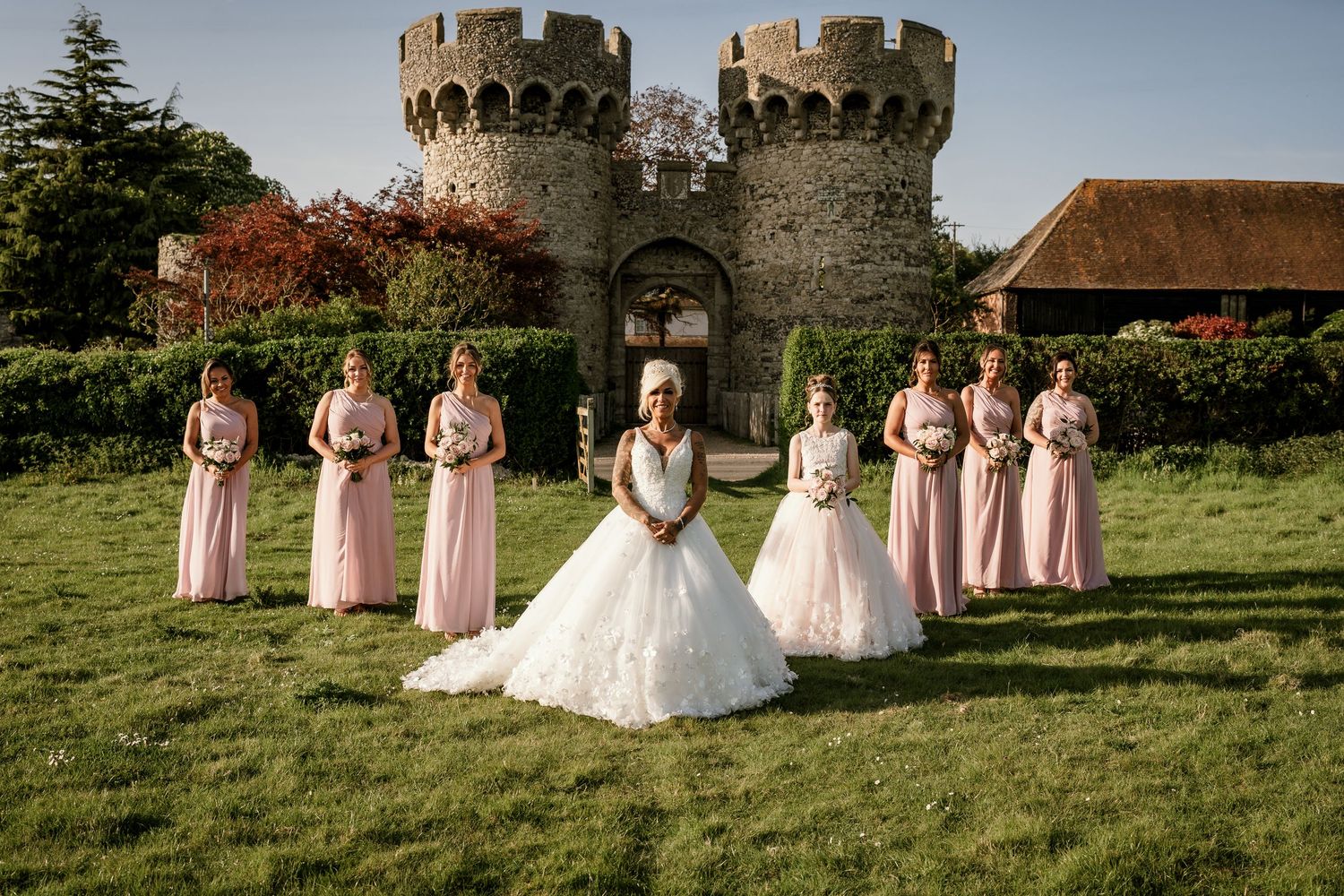 Wedding party poses in front of stone castle towers with bridesmaids in pink dresses.