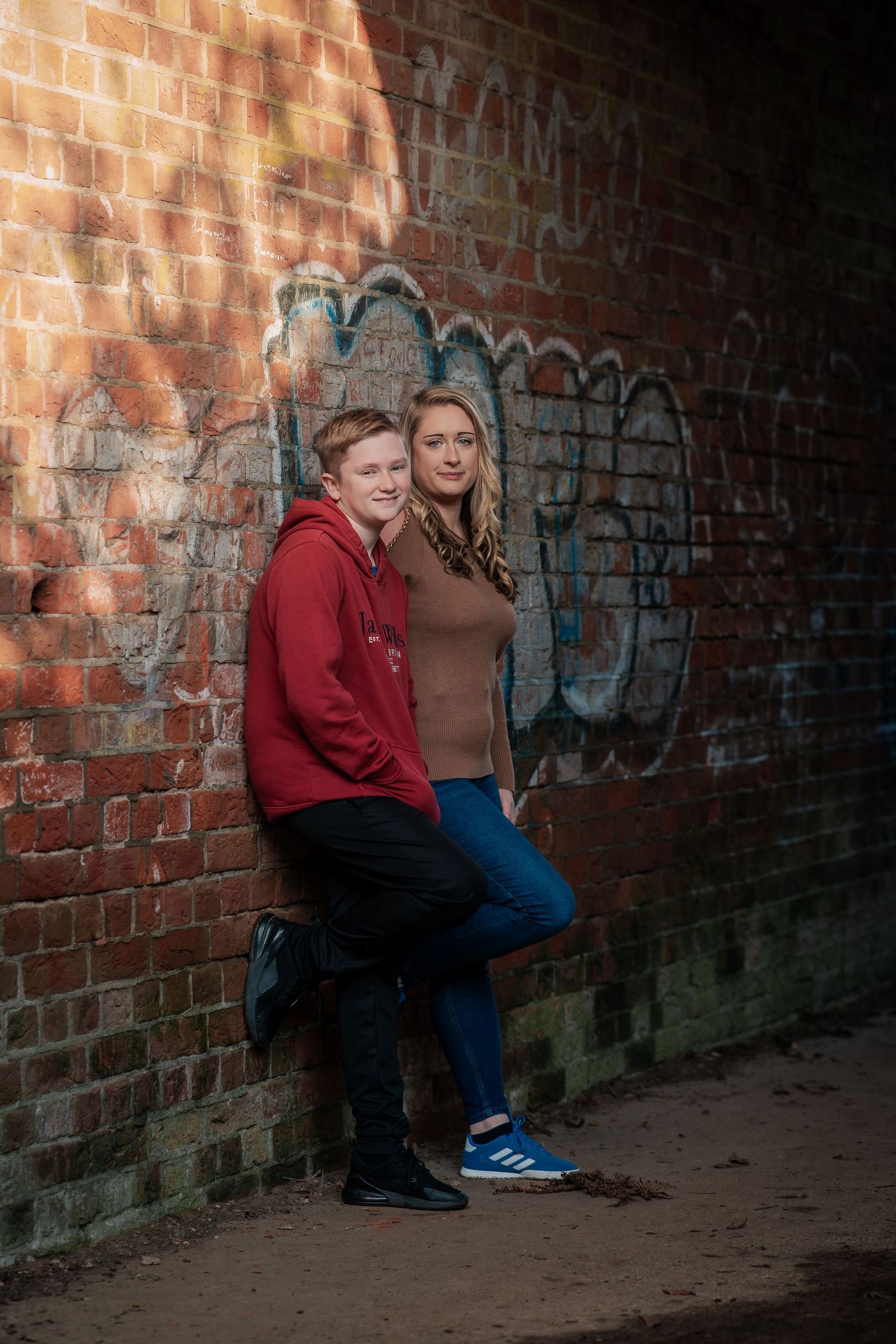 Couple sitting together against rustic brick wall with graffiti.