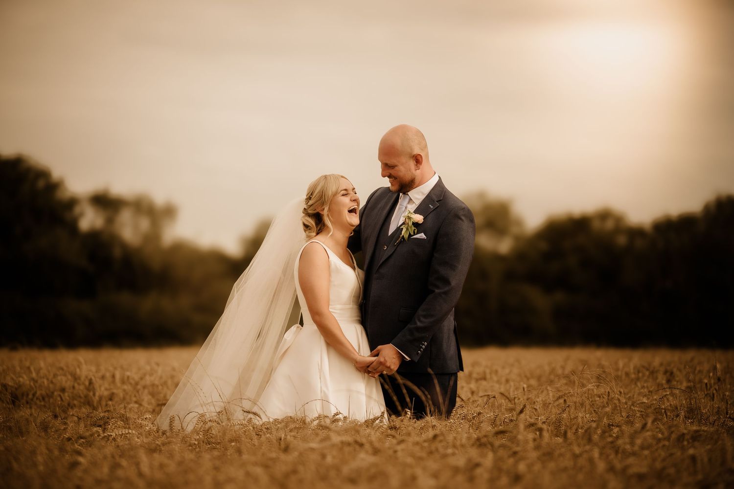 A wedding couple poses romantically in a golden wheat field at sunset.