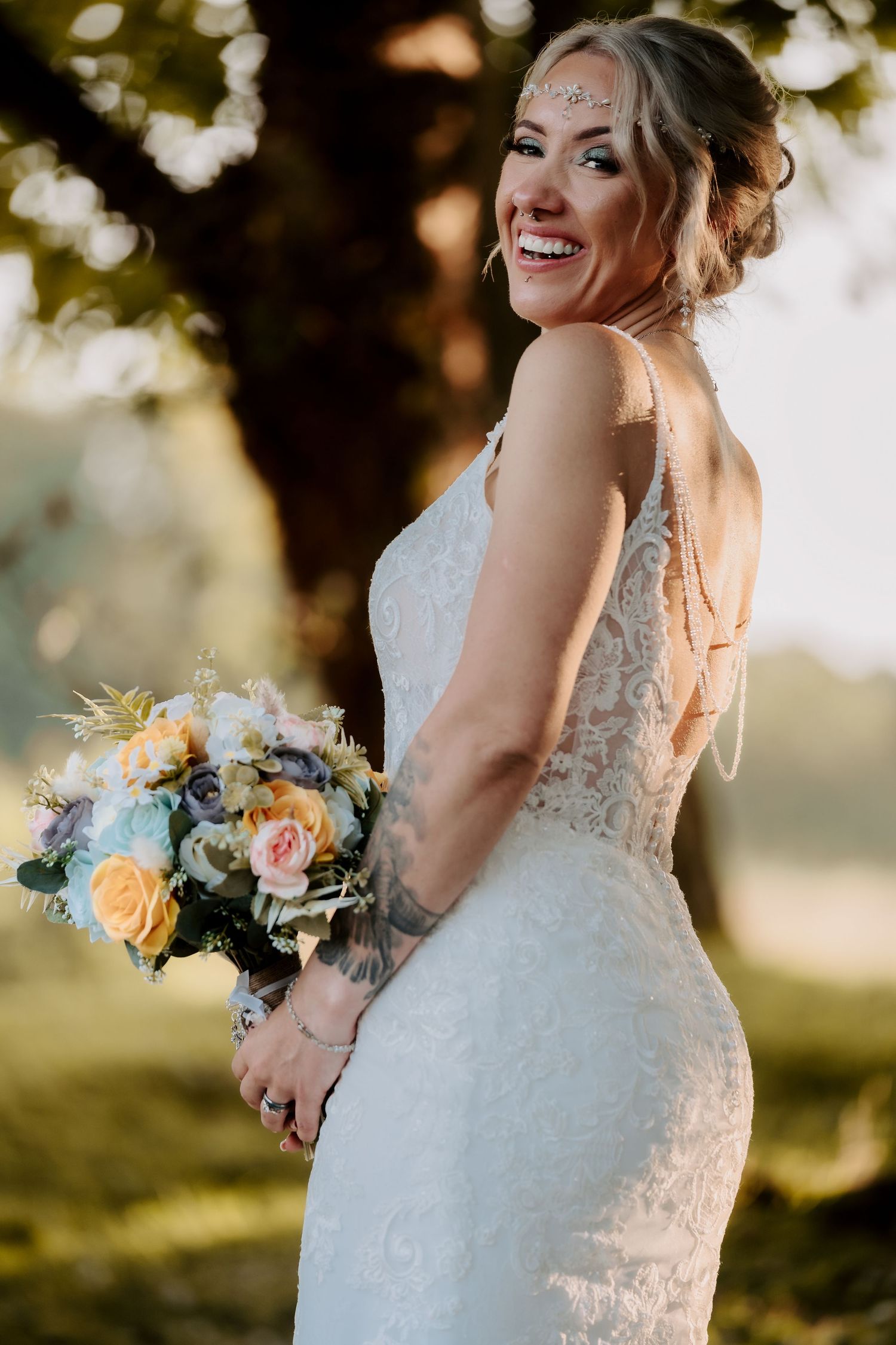 A bride in lace dress holds a pastel bouquet during golden hour.
