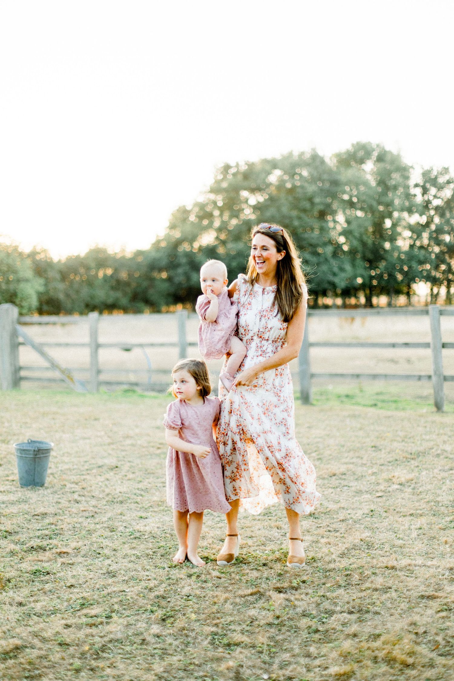 Family members in floral dresses share joyful moments together in a rustic field setting.