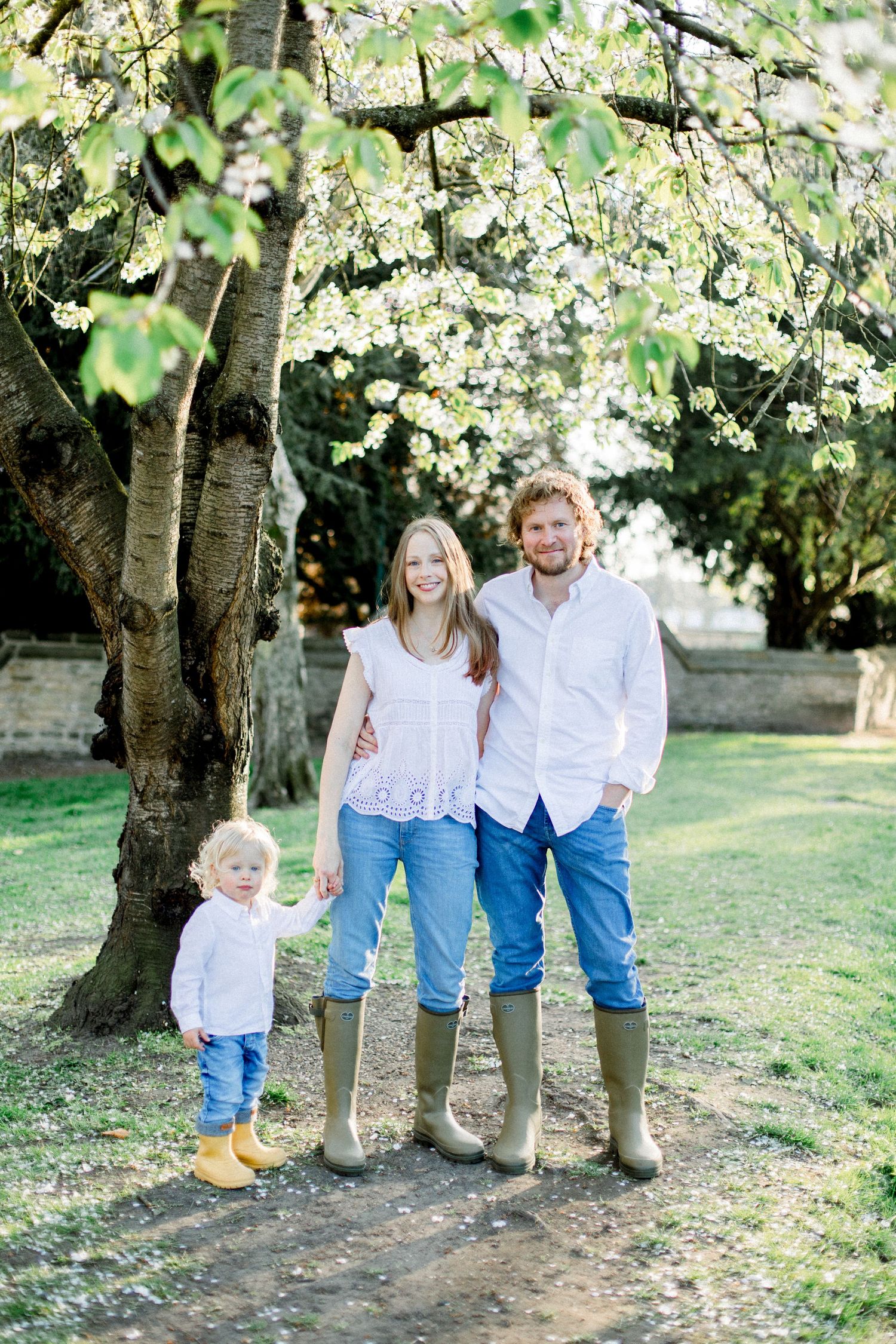 Family portrait under blooming spring trees wearing coordinated white and blue outfits.