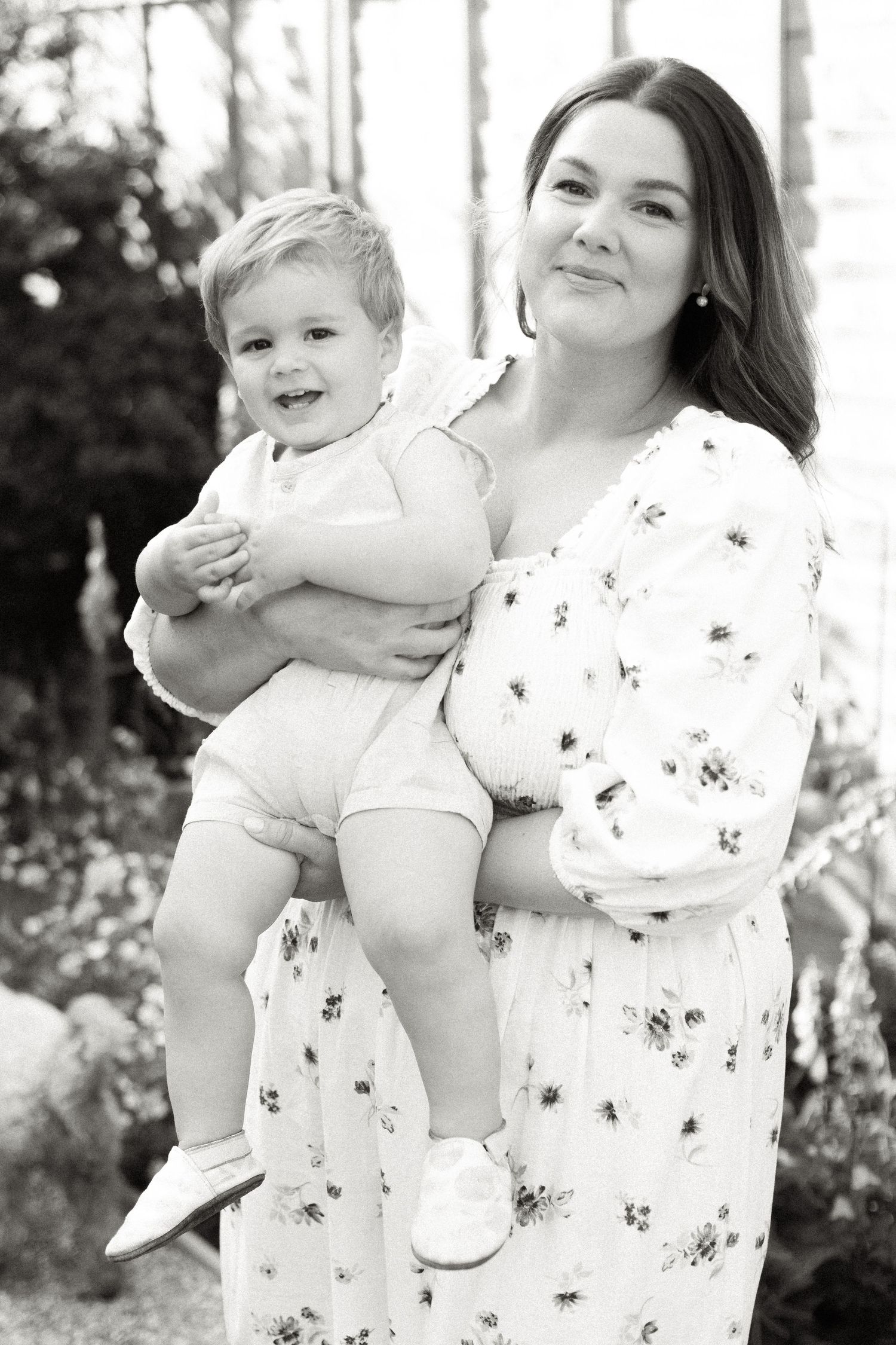 Portrait of a woman in a floral dress holding a small child outdoors.