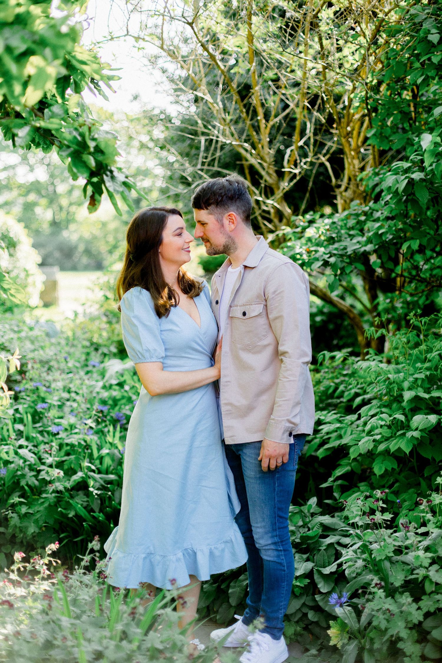 A romantic couple sharing intimate moments in a garden pathway surrounded by greenery.