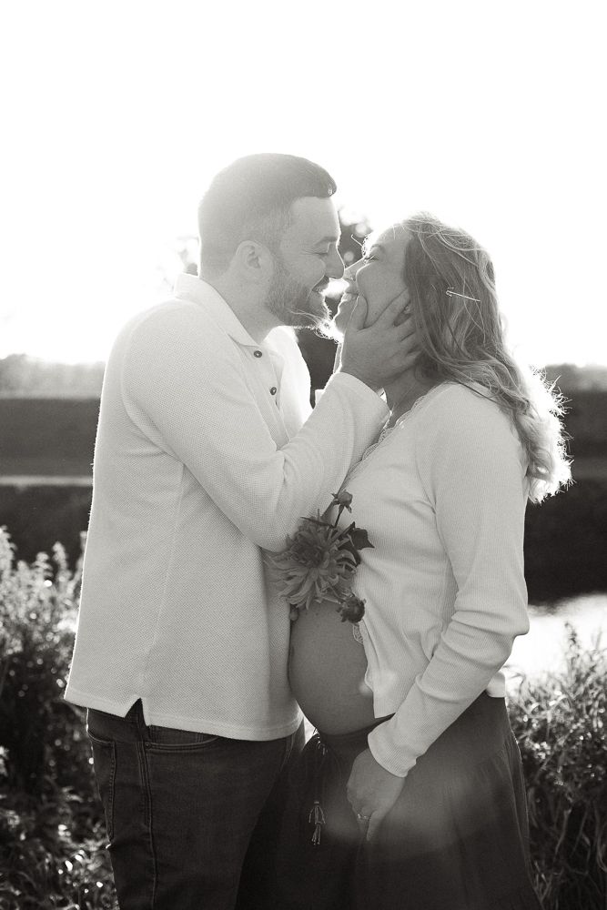 Black and white maternity photo of a couple sharing a tender moment outdoors, woman cradling baby bump.