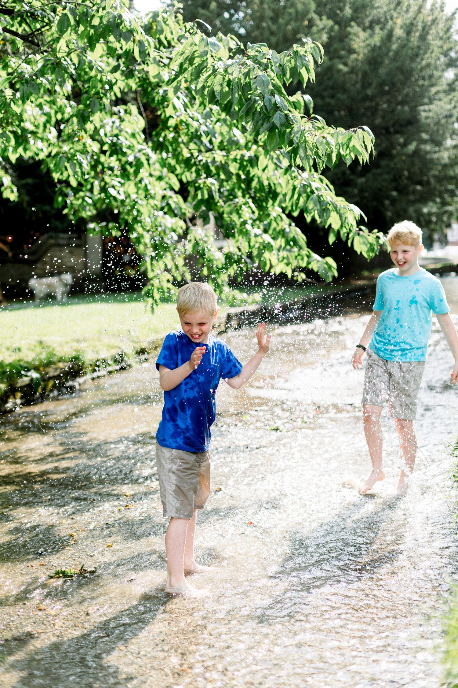 Children playing and splashing in a sprinkler on a sunny summer day in a backyard with green trees. Photography in East Yorkshire