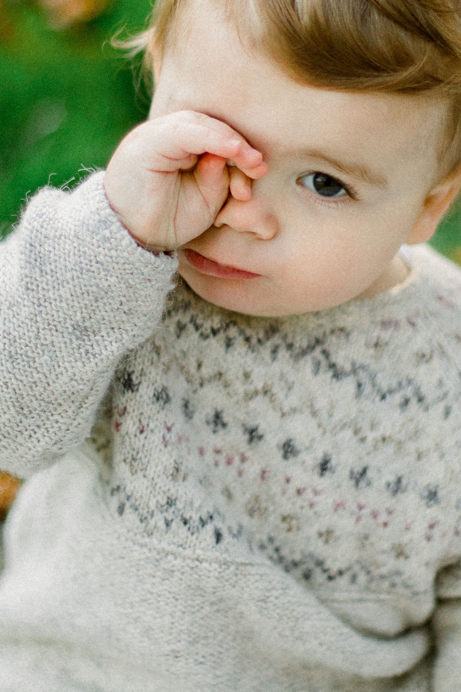 Close-up of a small child in a patterned sweater touching their nose.