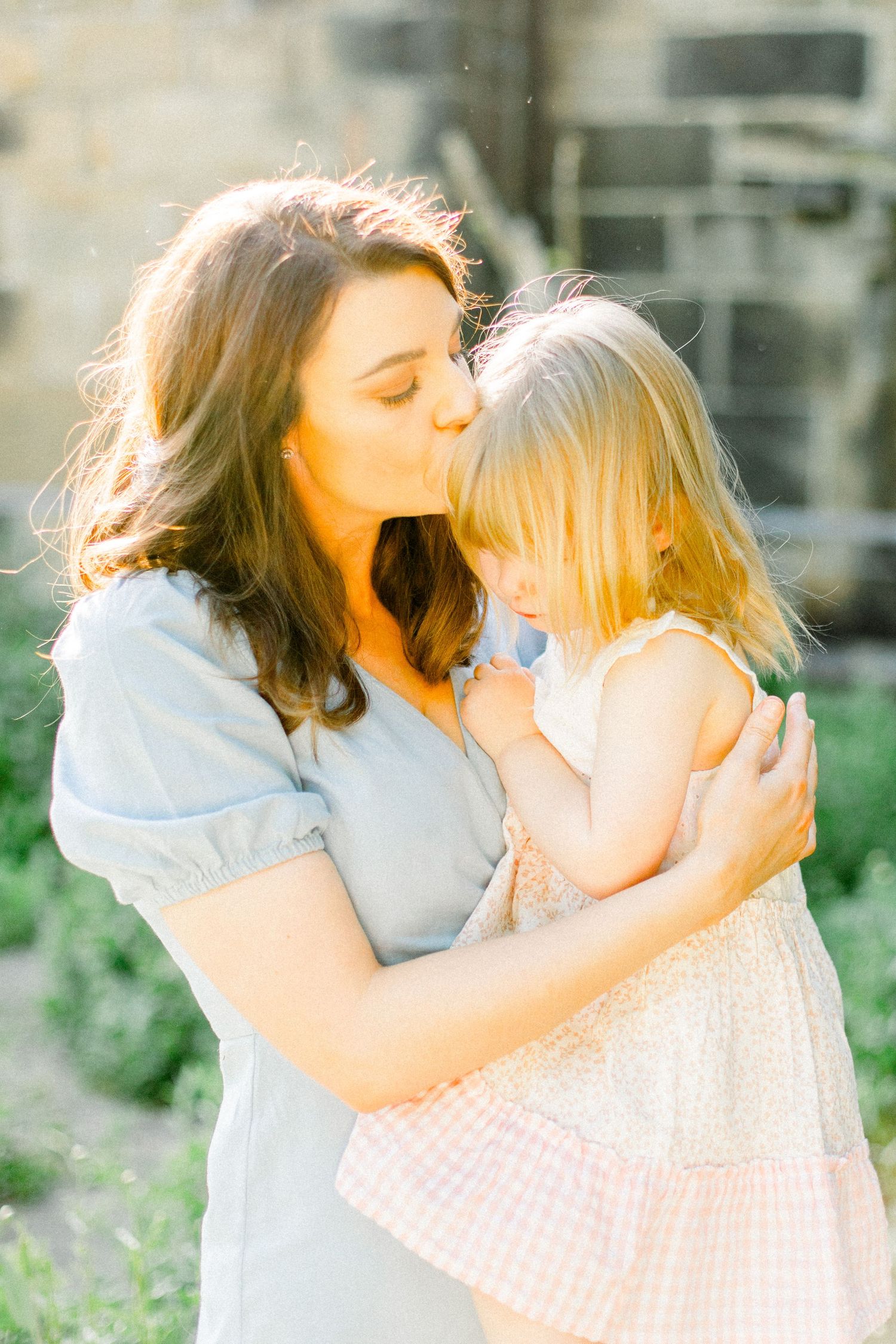 Tender moments captured in soft sunlight against stone wall background.