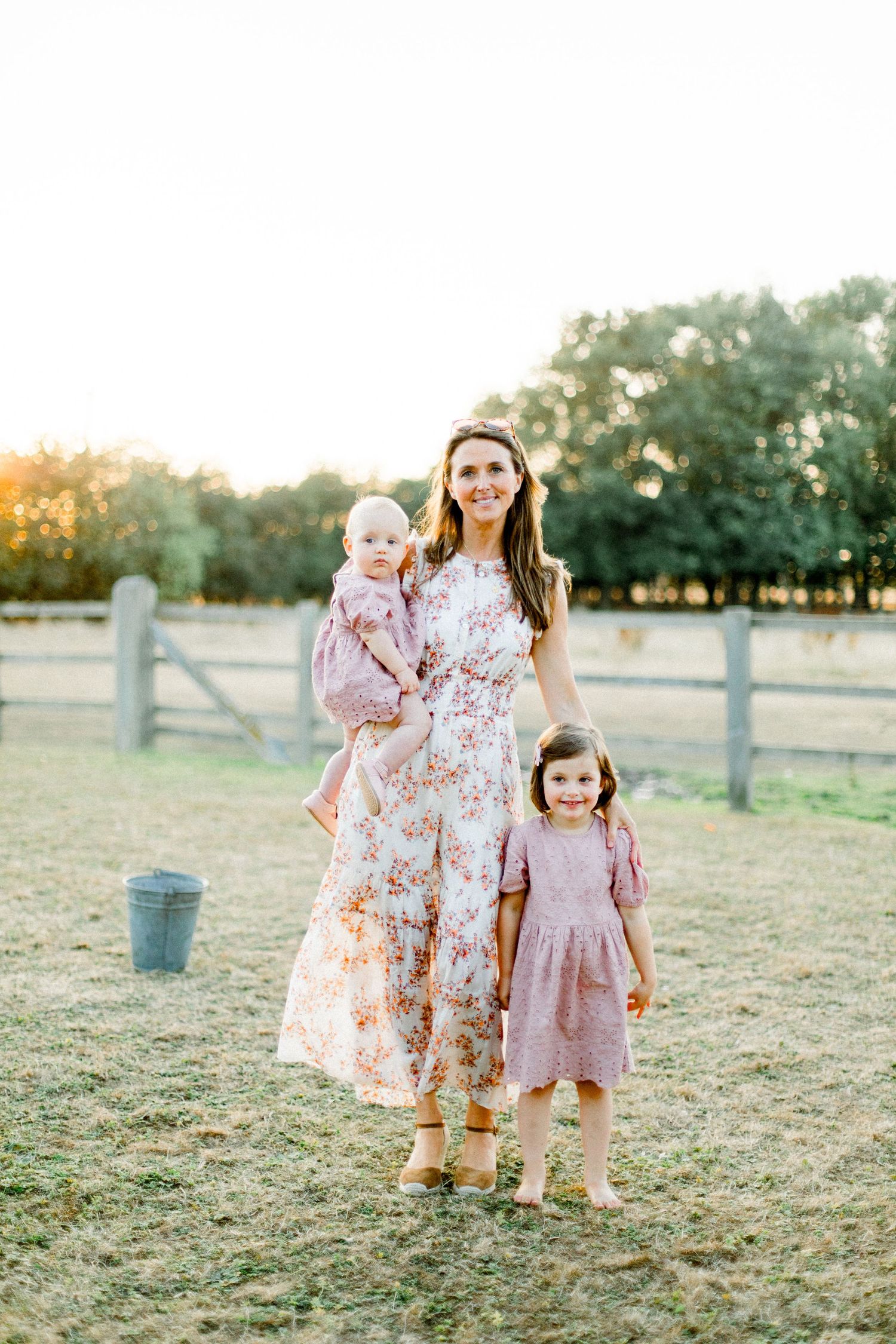 Children in vintage-style dresses play in a rustic farm setting at sunset.