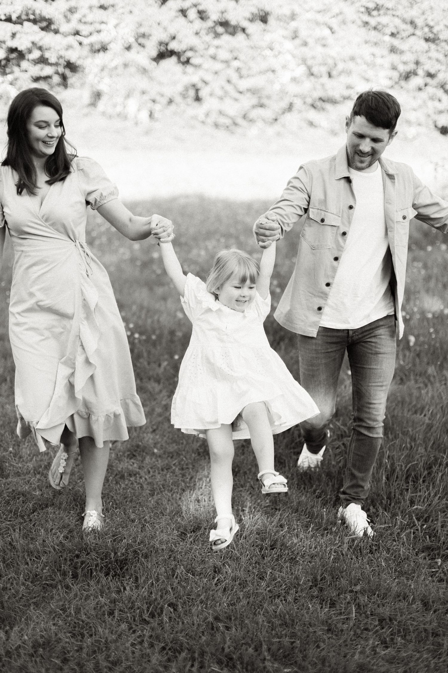 Joyful family running and playing together in a grassy field wearing light summer clothing.