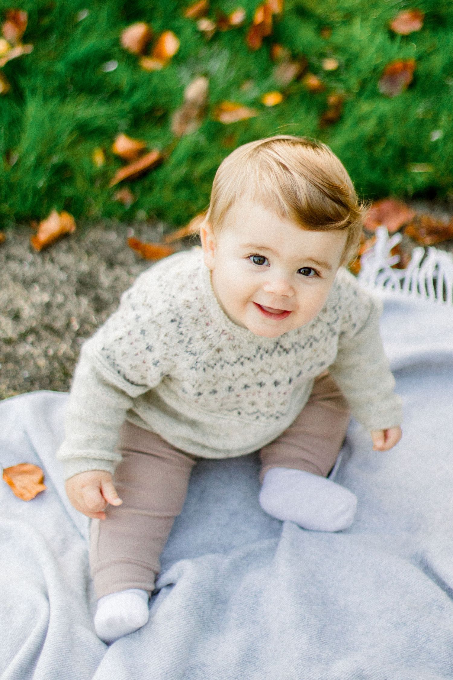 Baby wearing cream knit sweater sitting on light blue blanket outdoors.
