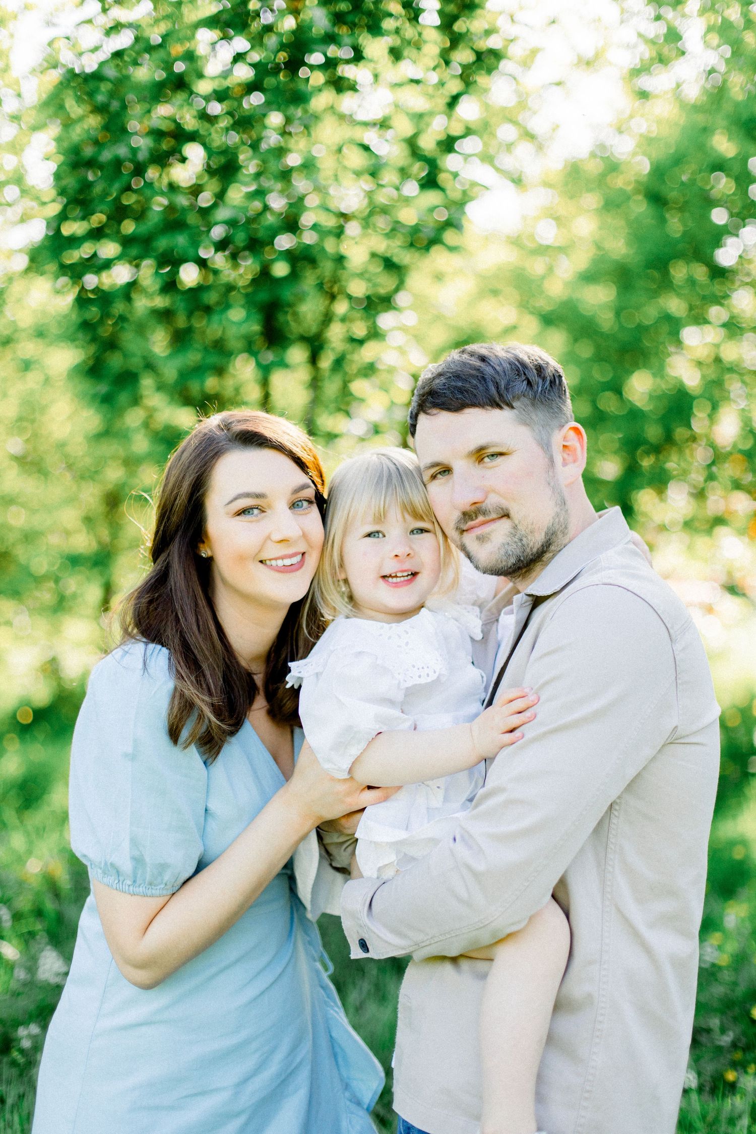 A happy family portrait session captured in a sunlit garden setting.