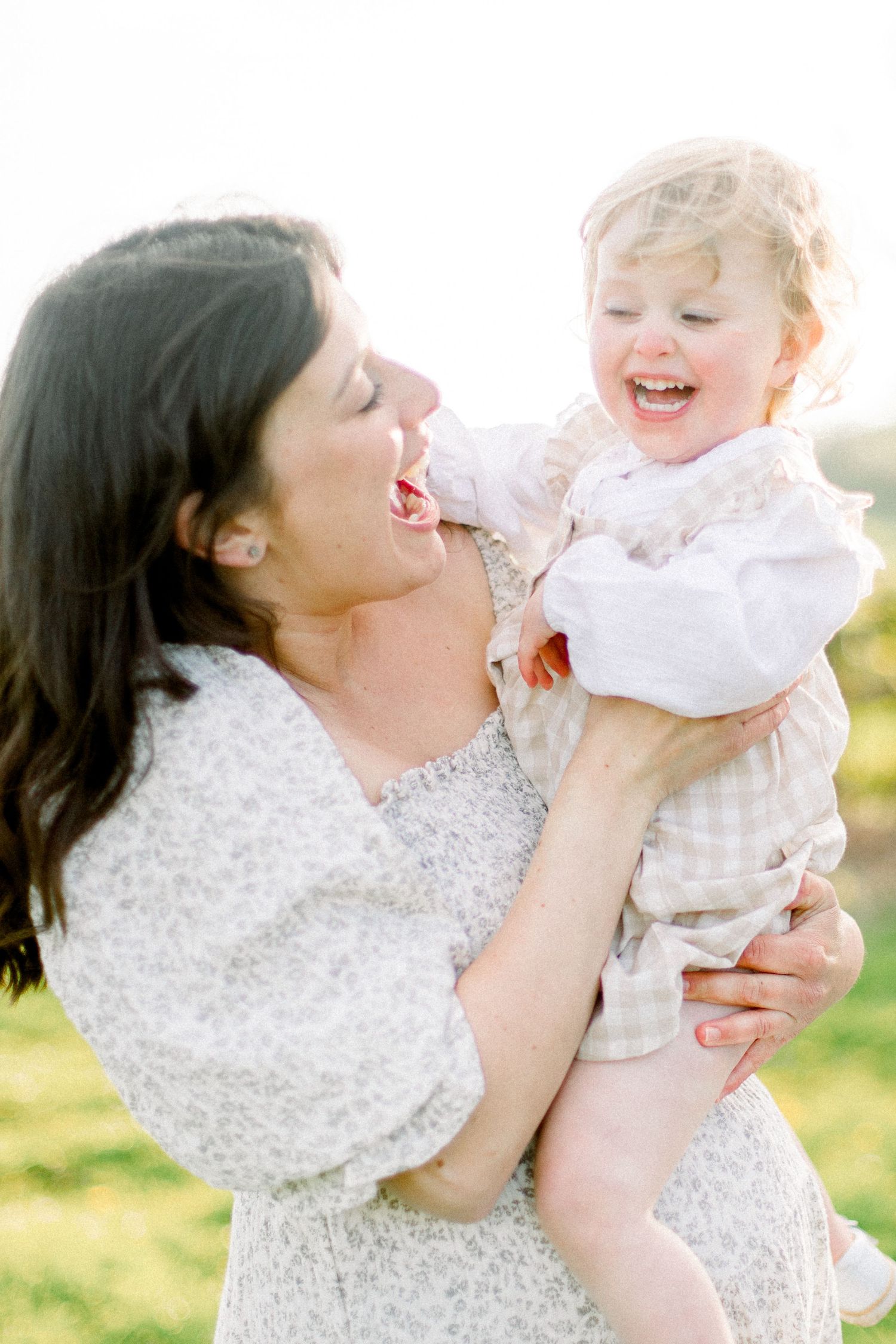 A joyful moment between parent and child outdoors in white dresses.