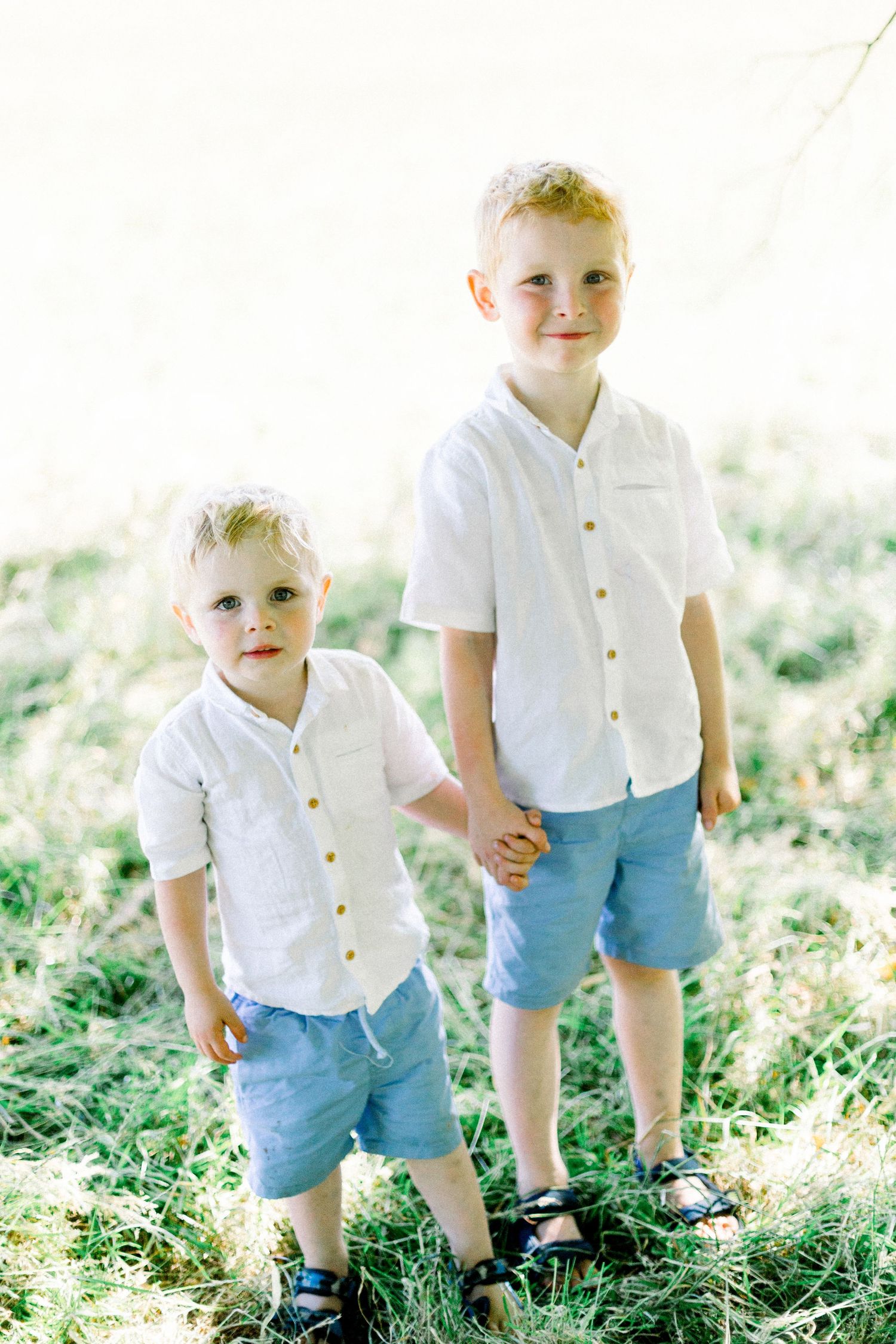 Child in white button-down shirt and blue shorts walking through sunny grass.
