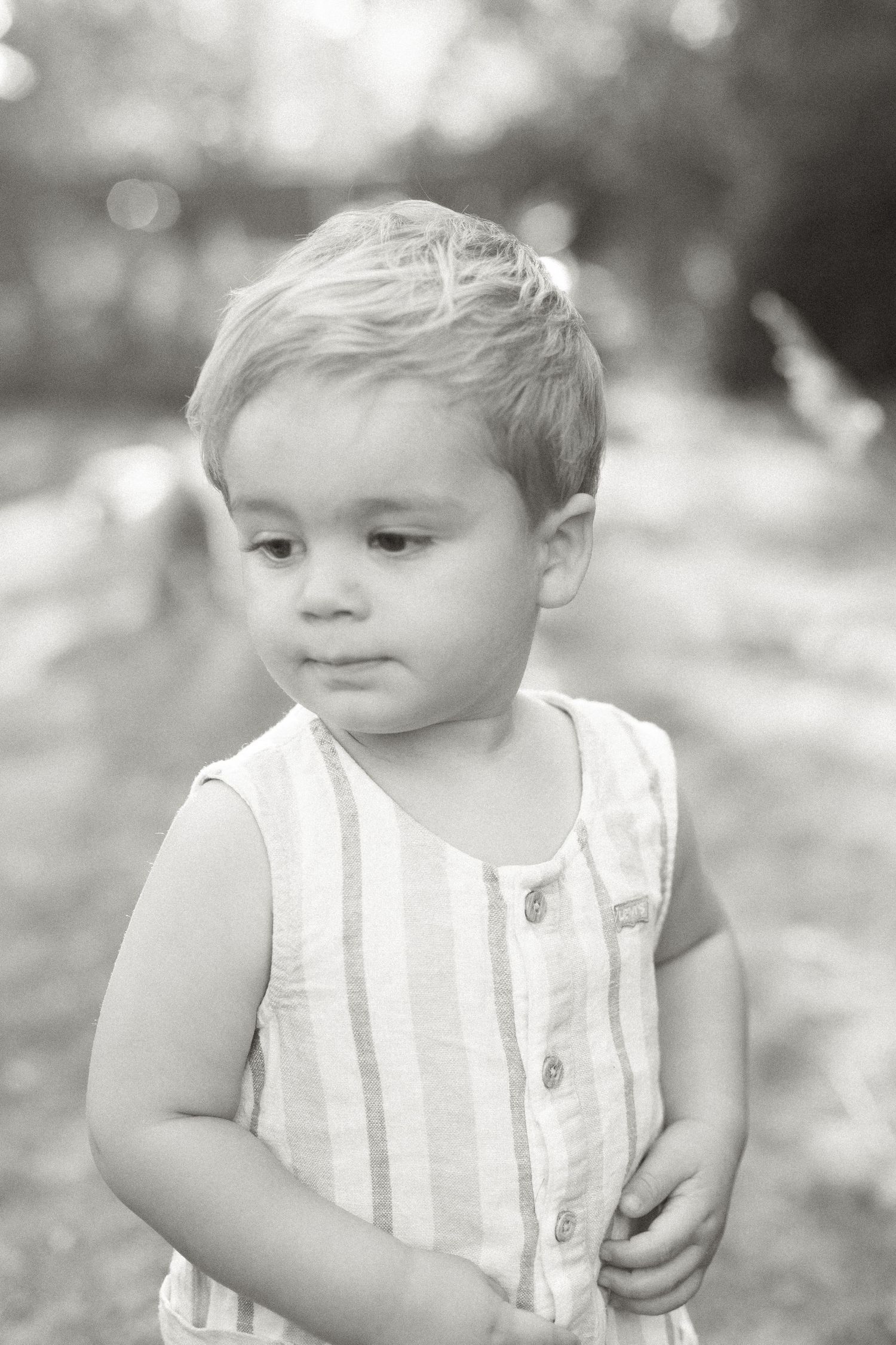 Black and white portrait of a child in striped sleeveless romper looking to the side.