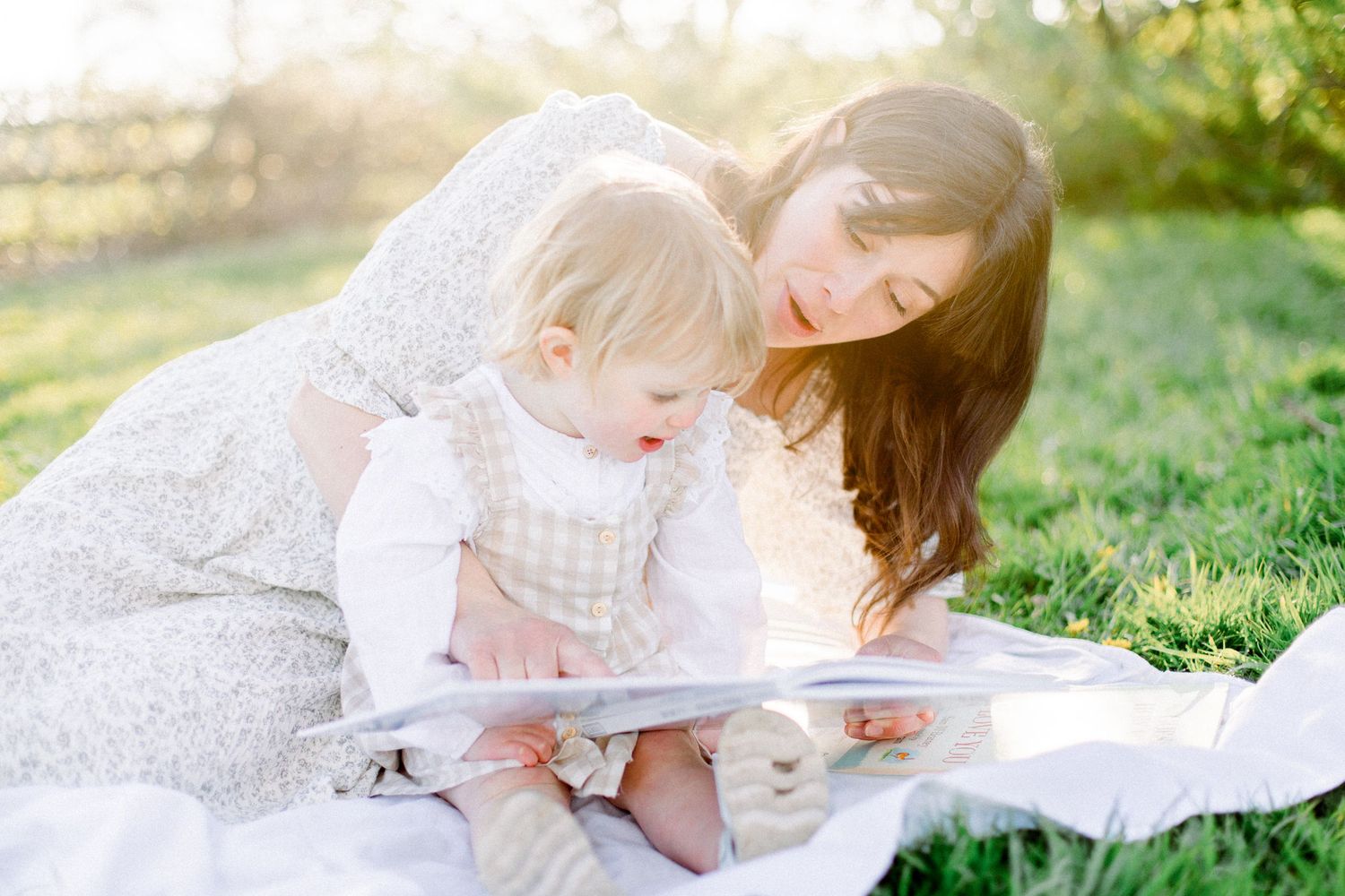 A peaceful outdoor reading scene with people gathered on a white blanket in natural light.