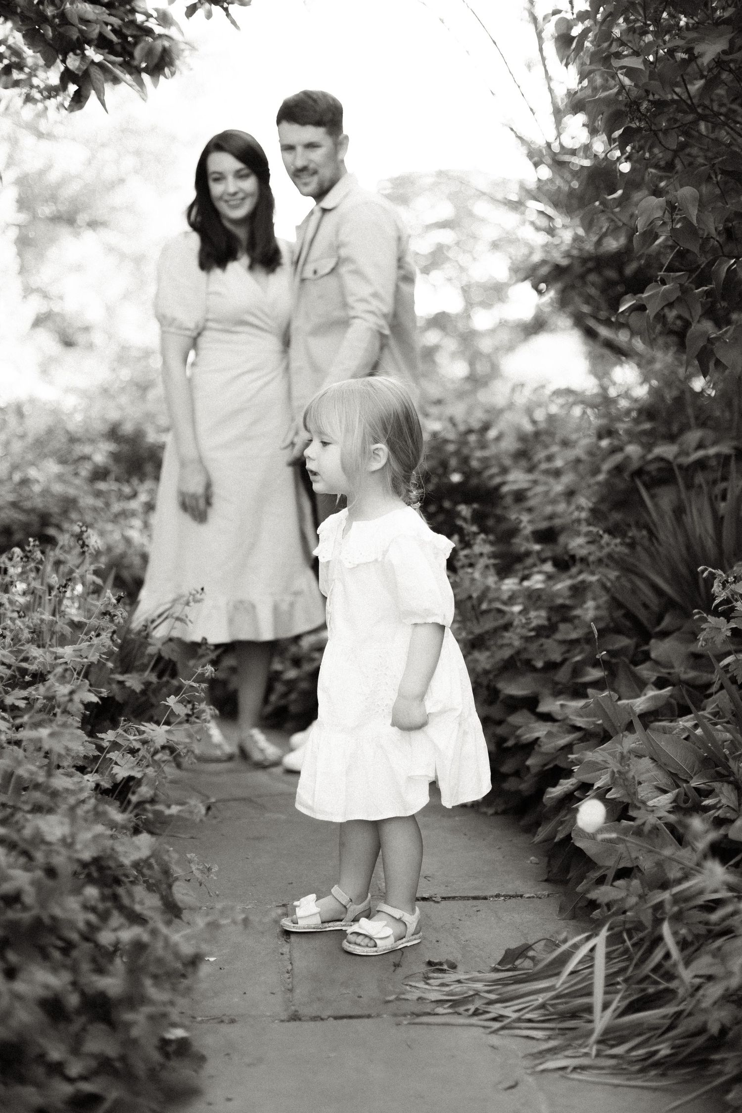 Black and white family portrait on a garden path surrounded by lush foliage.