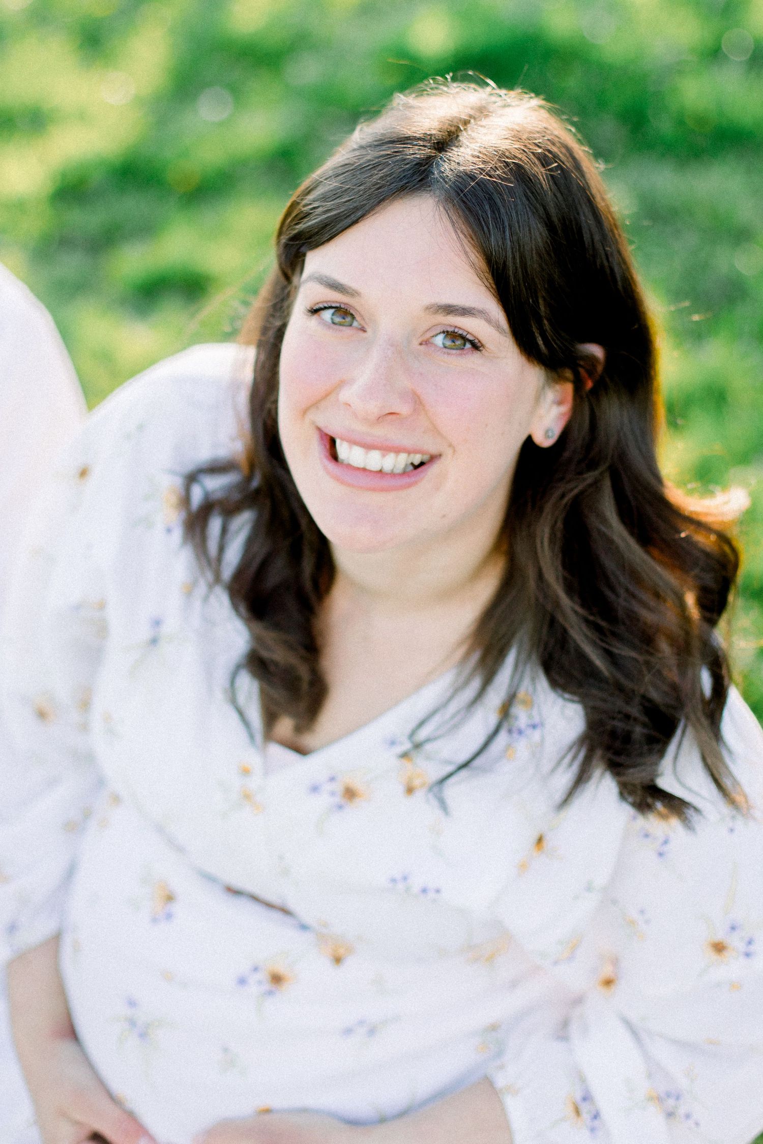 Woman in white dress smiles during outdoor spring photoshoot.