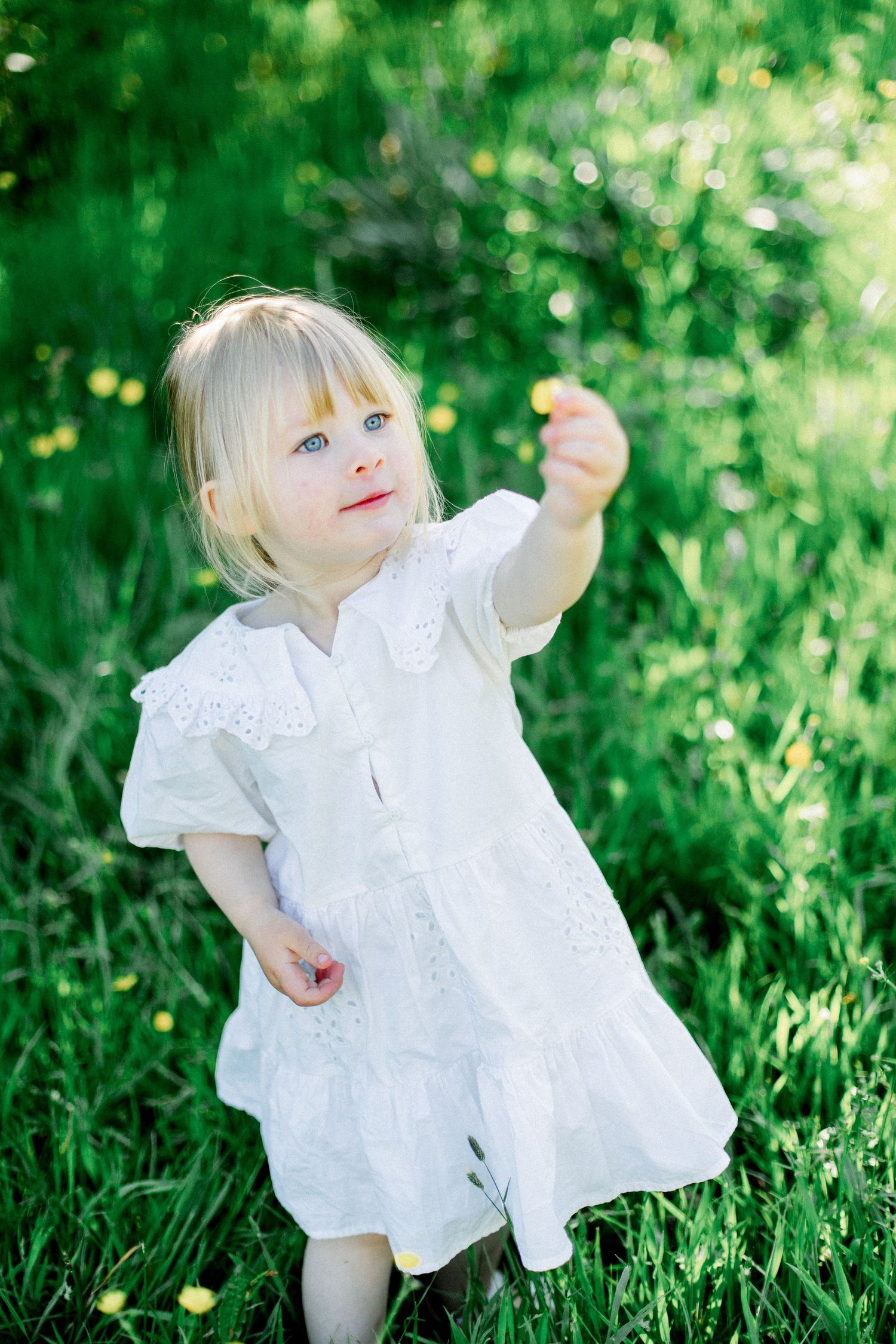 A small figure in white plays joyfully in the grass on a sunny day.