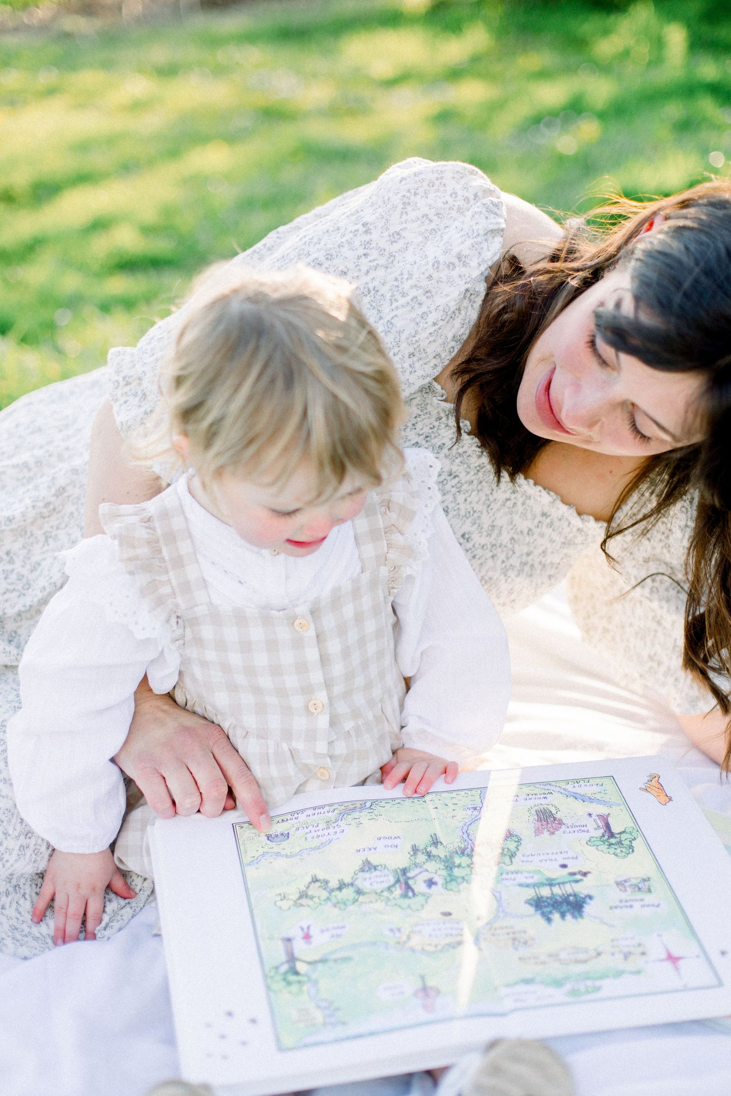 Mother and toddler reading a colorful picture book together on a blanket in a sunny green park.
