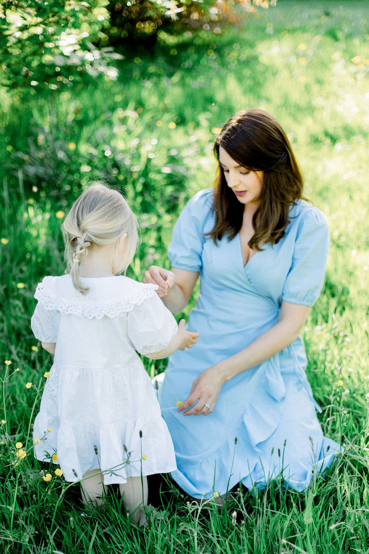 A light blue dress and white dress create a sweet outdoor scene in lush green grass.