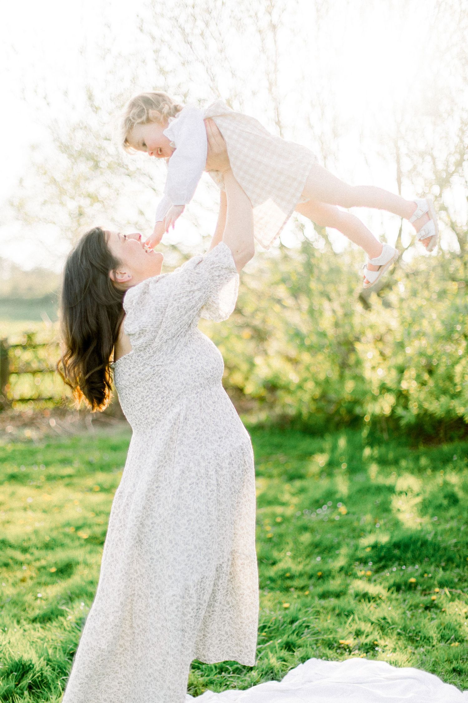 Joyful outdoor portrait with sunlit garden backdrop showing playful lift pose.