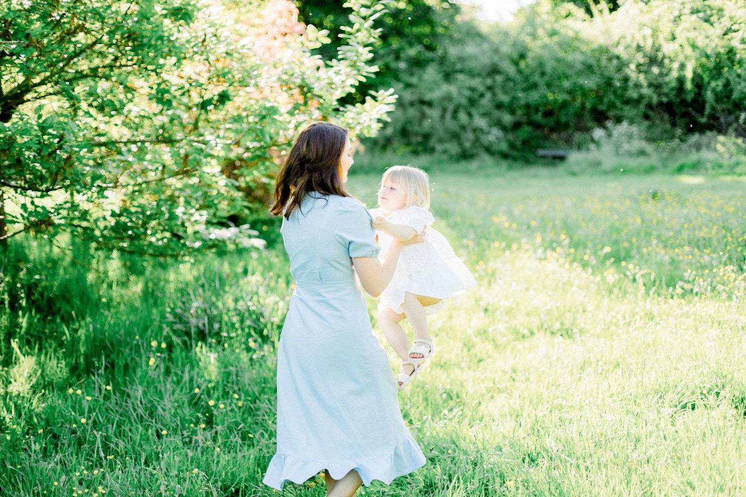 A couple in white outfits walks together through a lush green meadow on a sunny summer day.