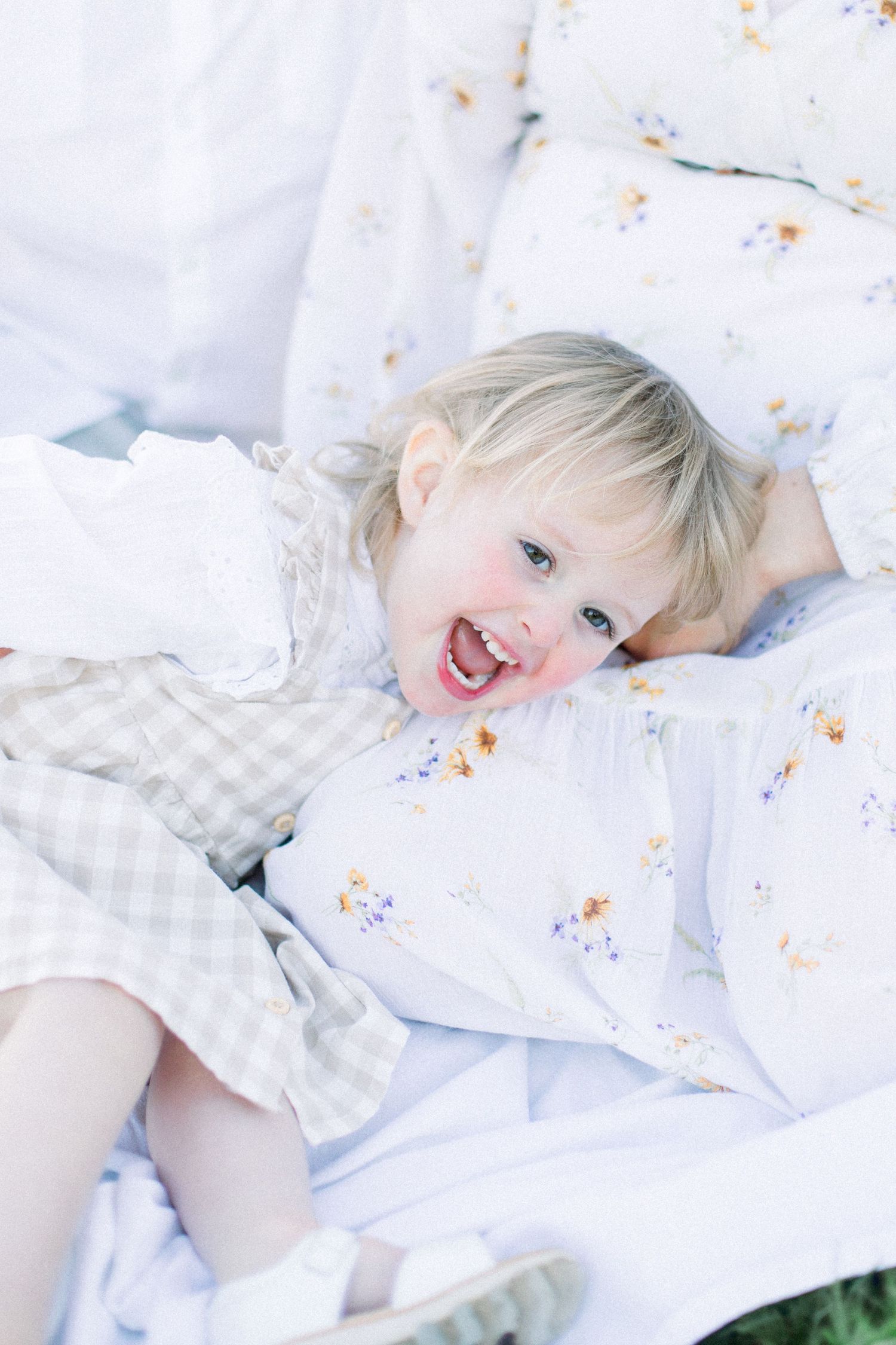 Child in white clothing lies on blanket during outdoor photo session.