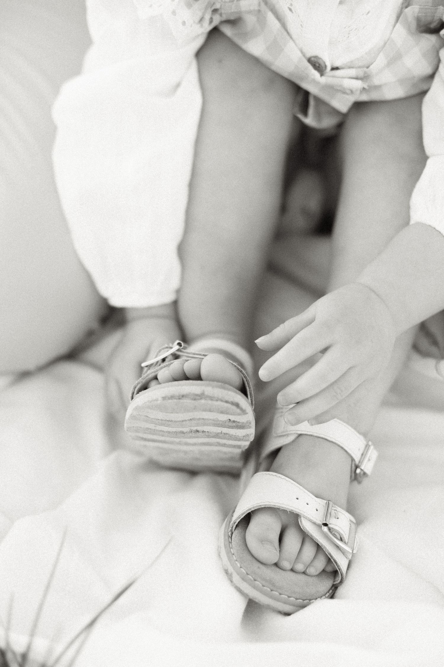 Close-up black and white photo of tiny feet wearing white buckle sandals.