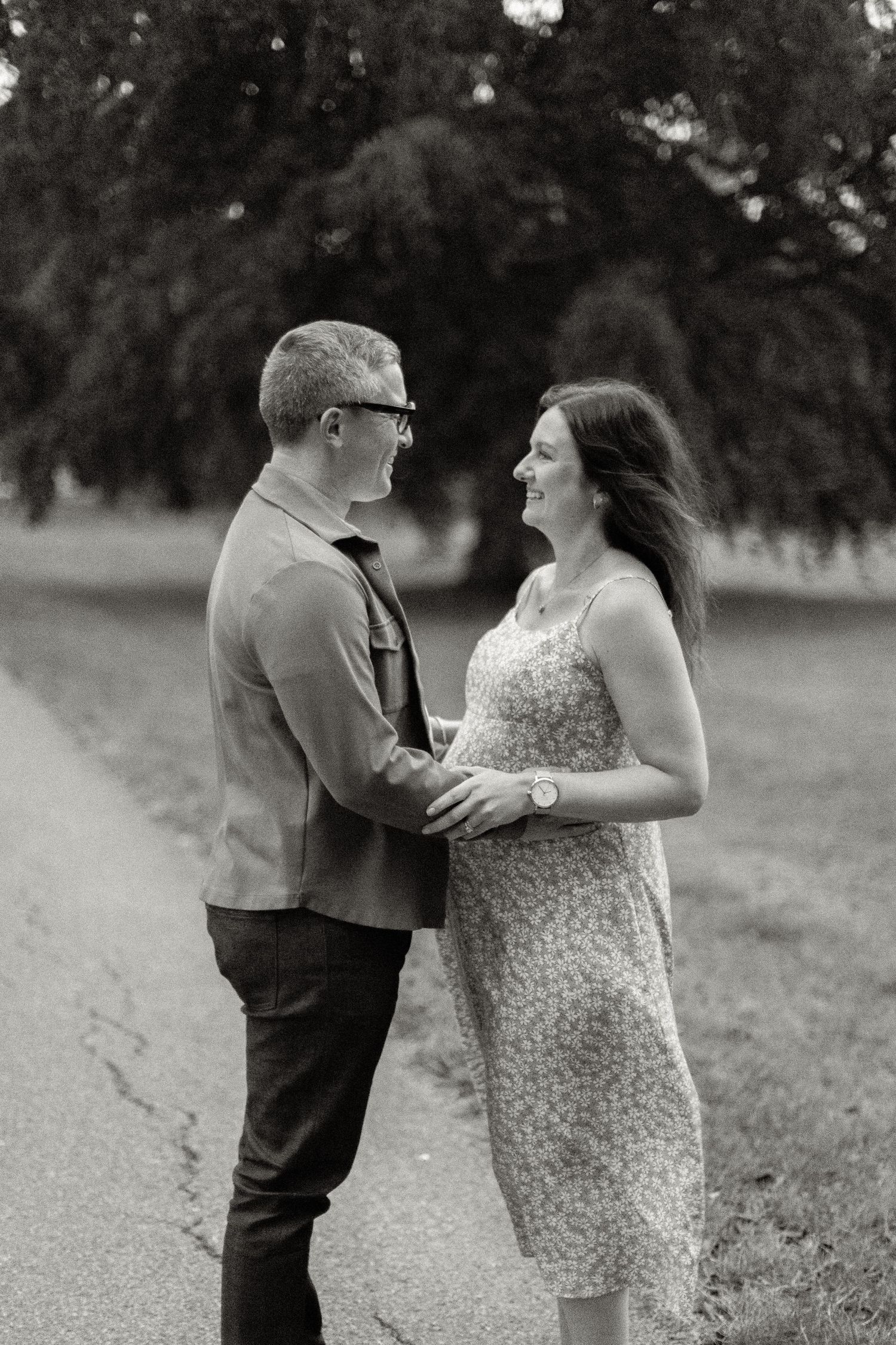 Black and white photo of couple holding hands and smiling at each other in a park.