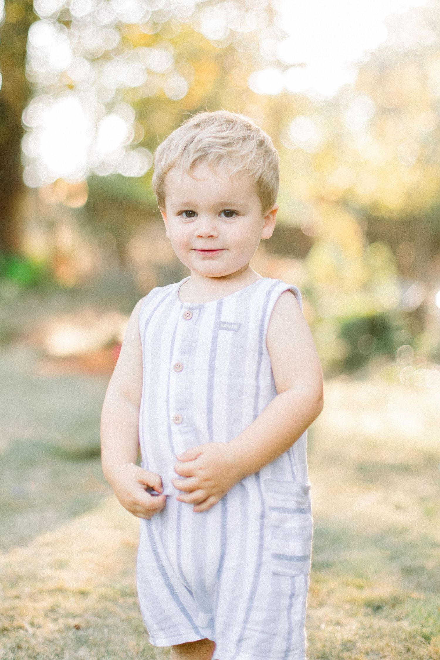 Child wearing a light striped sleeveless romper standing in golden sunlight.