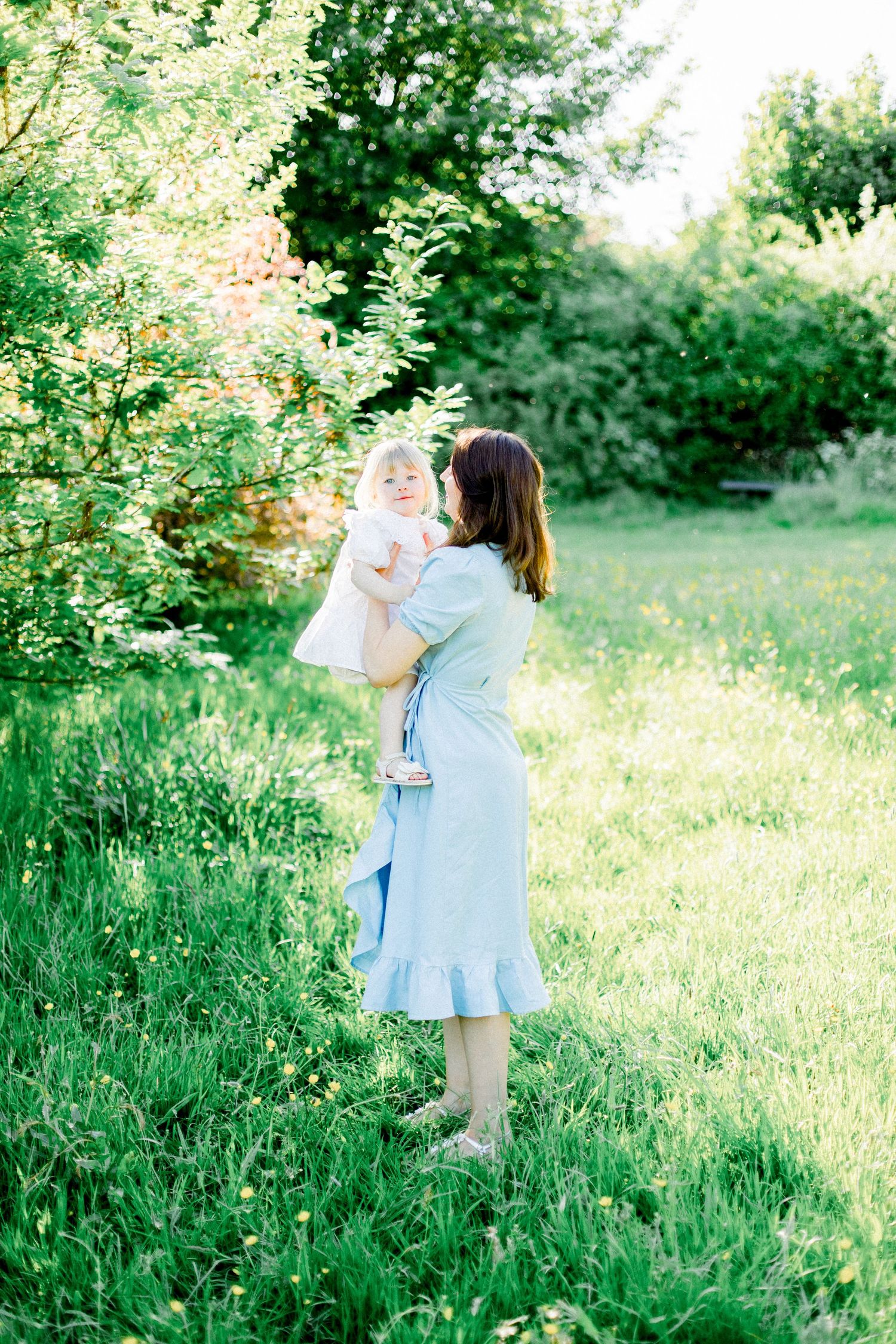 Mother and child sharing playful moments in a sunlit meadow with tall grass.