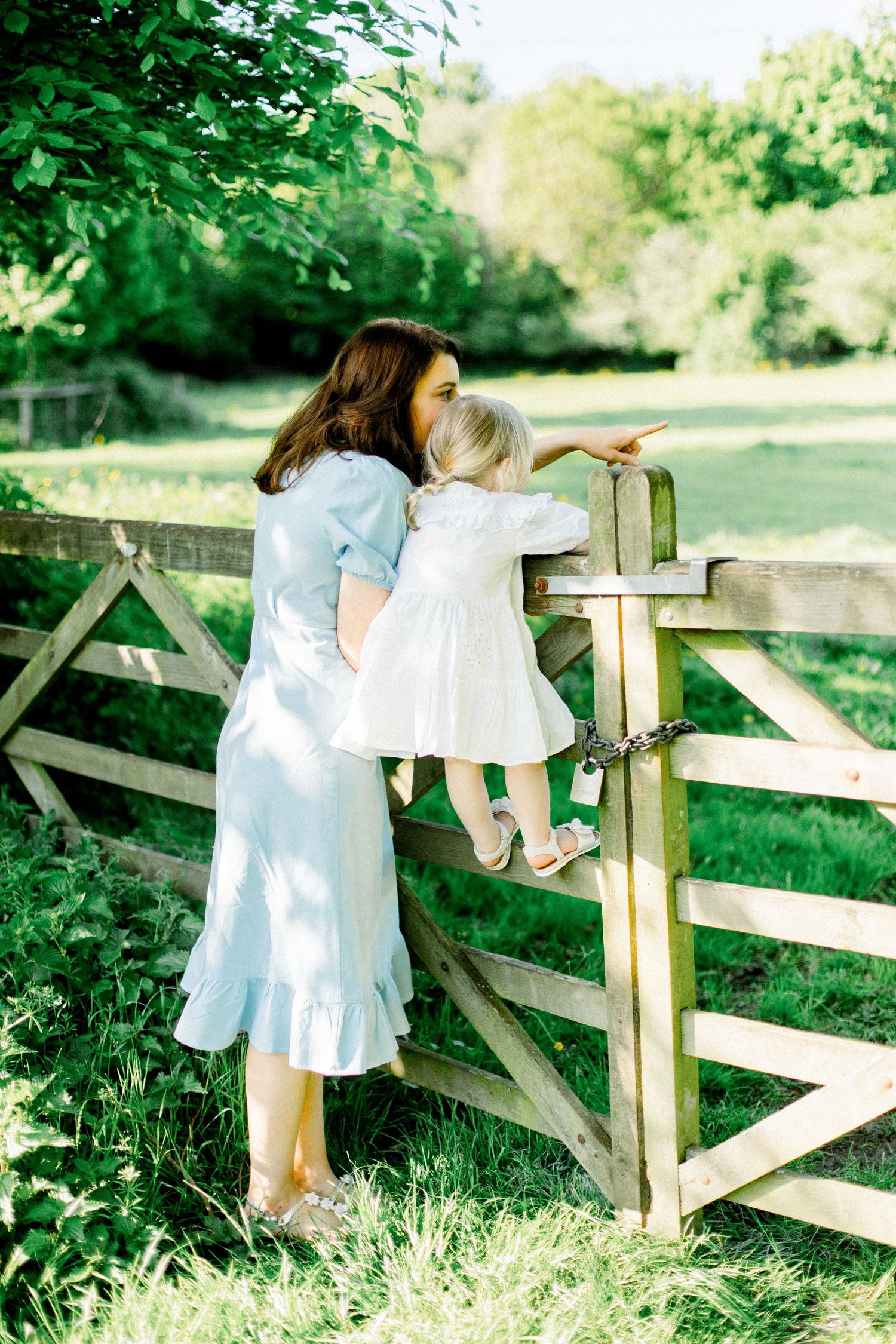 Dreamy springtime scene with white dresses and wooden fence in lush green garden setting.