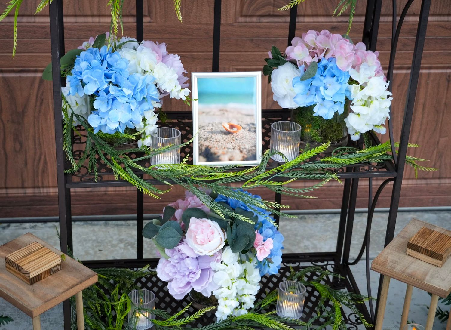 Heart-shaped wreath with blue and pink hydrangeas framing a beach photo on decorative metal display rack.