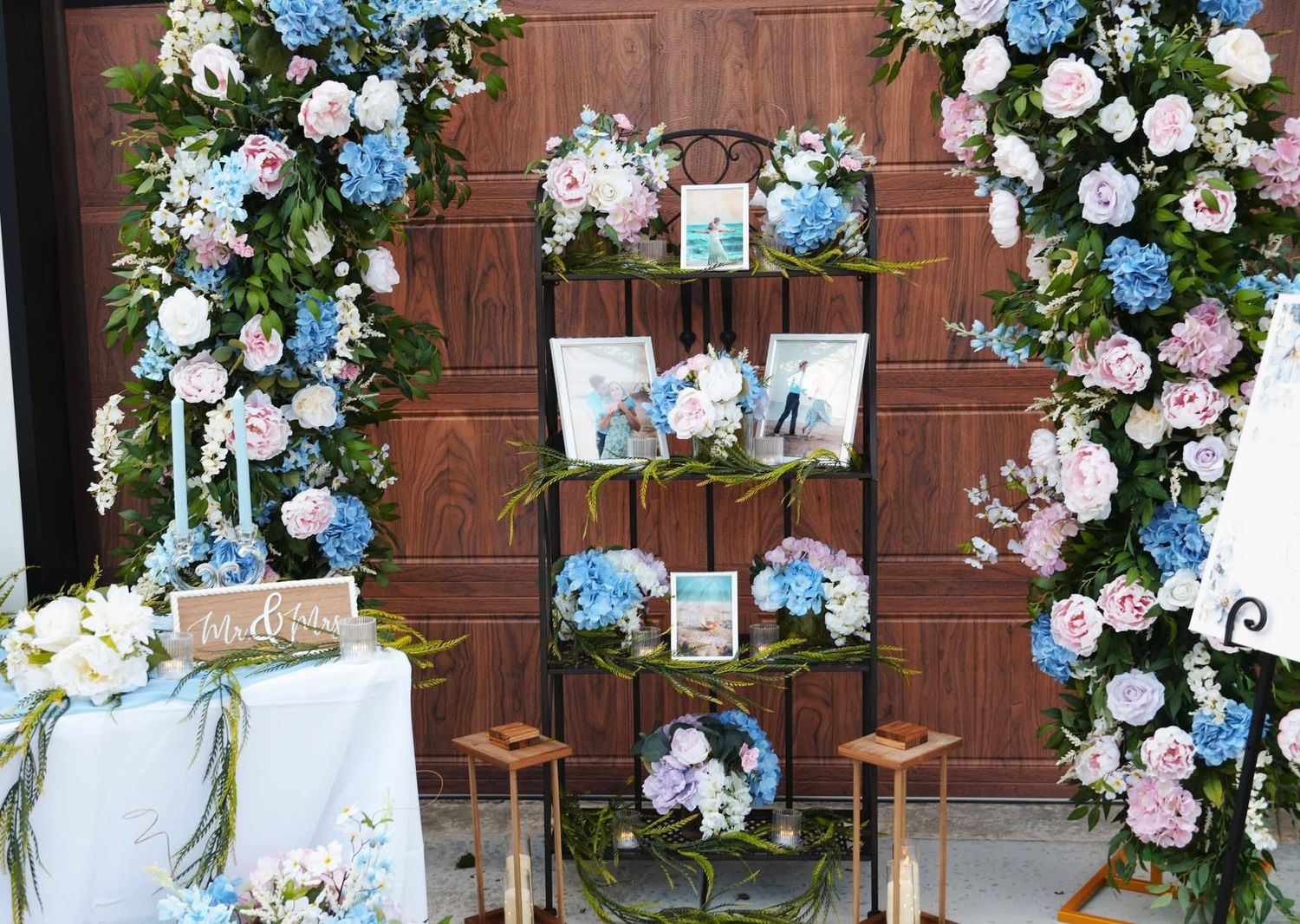 Outdoor wedding seating chart display with pink and blue hydrangea floral arrangements on wooden ladder shelf.