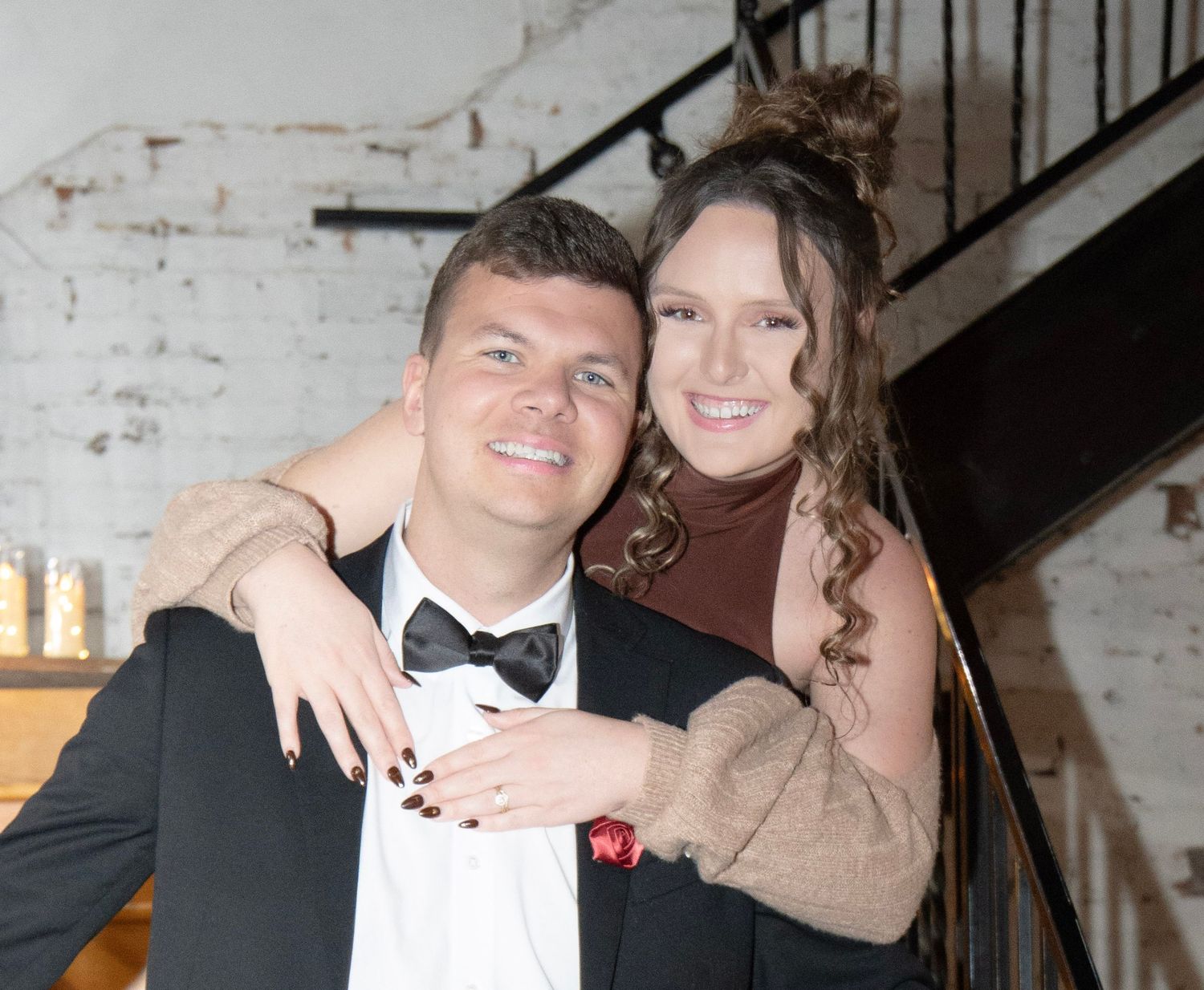 Smiling couple posing together indoors near a staircase, dressed in formal attire for a wedding reception.