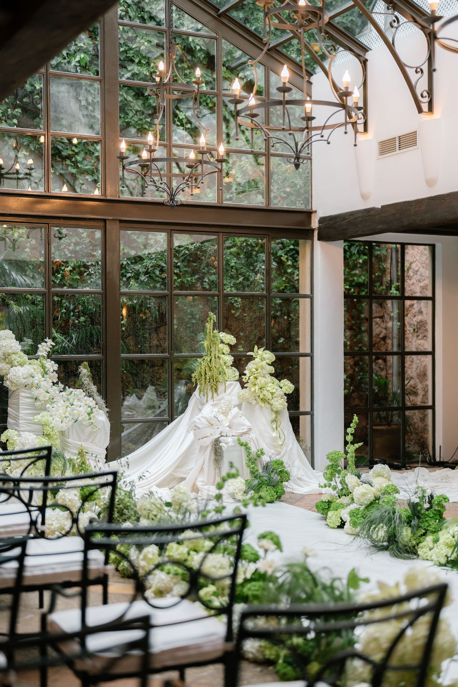 Wedding ceremony space in conservatory with black chairs and white floral aisle decorations.