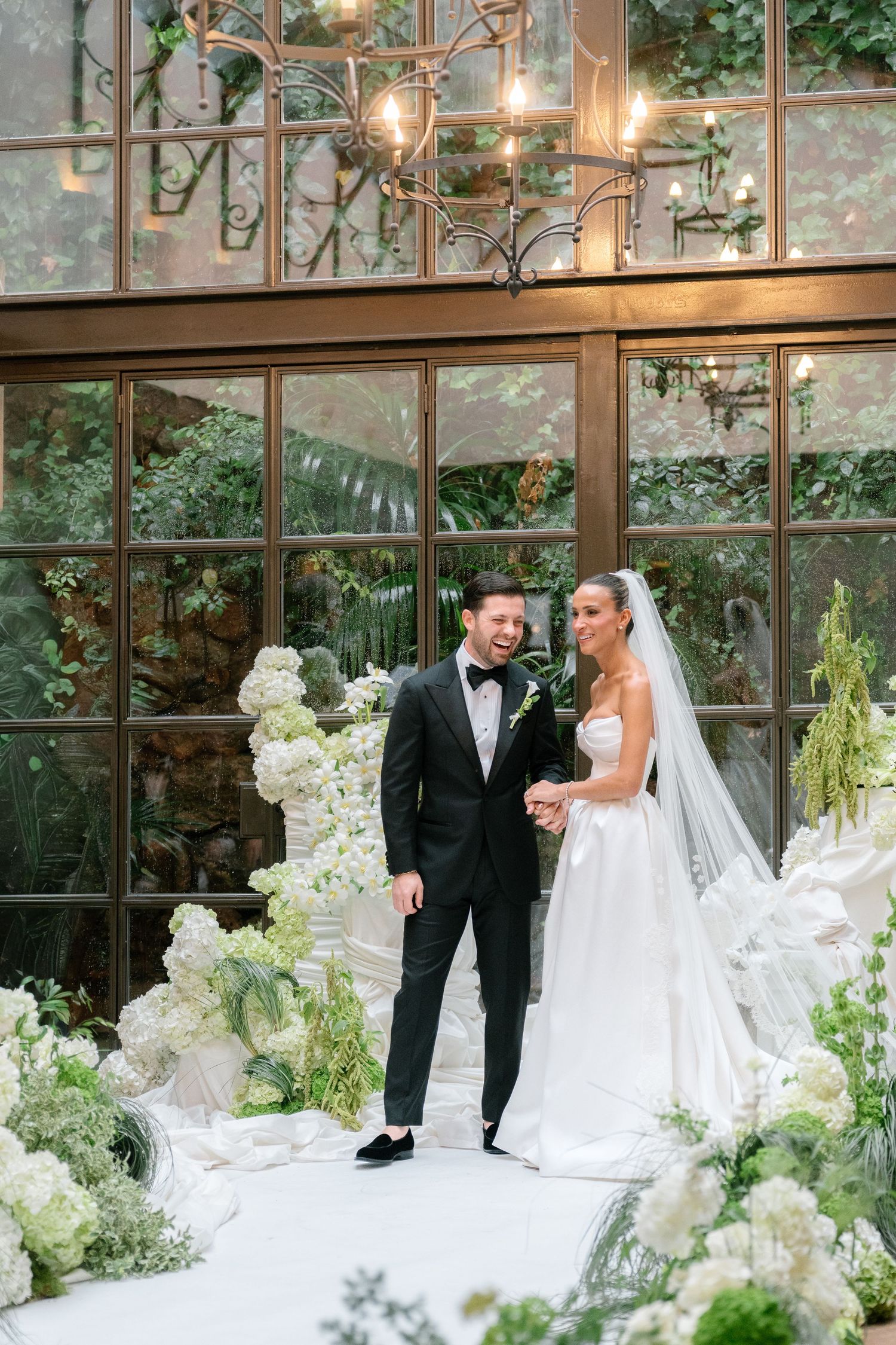 An elegant wedding reception setup with white floral arrangements and glass windows in a conservatory-style venue.