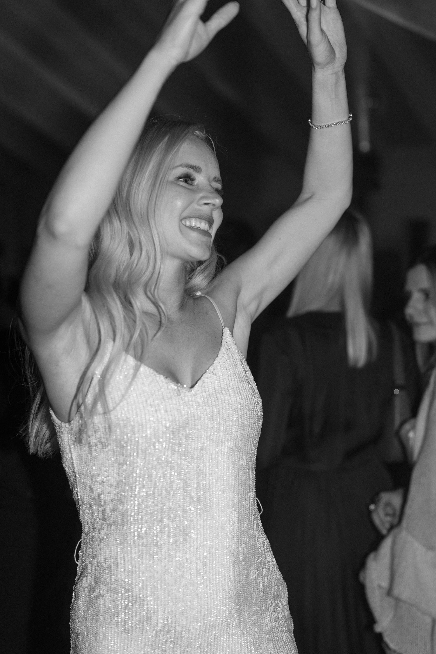 A joyful bride dancing with raised arms in a sparkling white dress at a wedding reception.