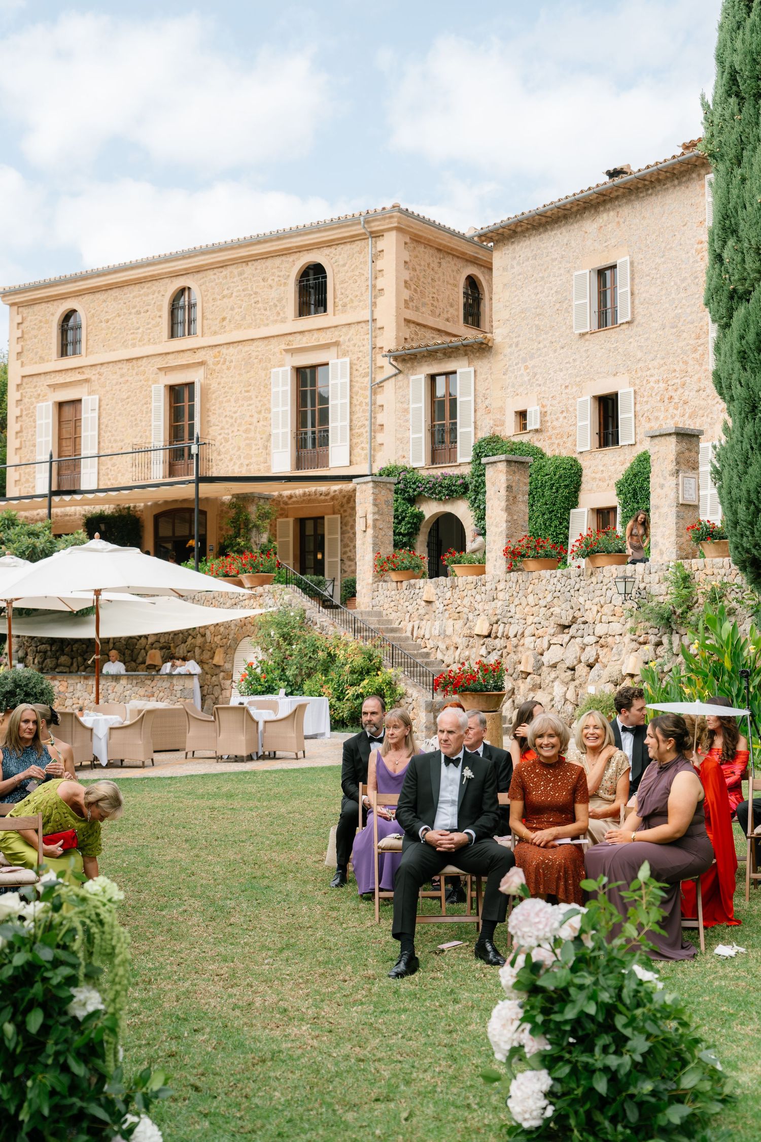 Wedding guests gathered on the lawn of a rustic stone villa during an outdoor reception.