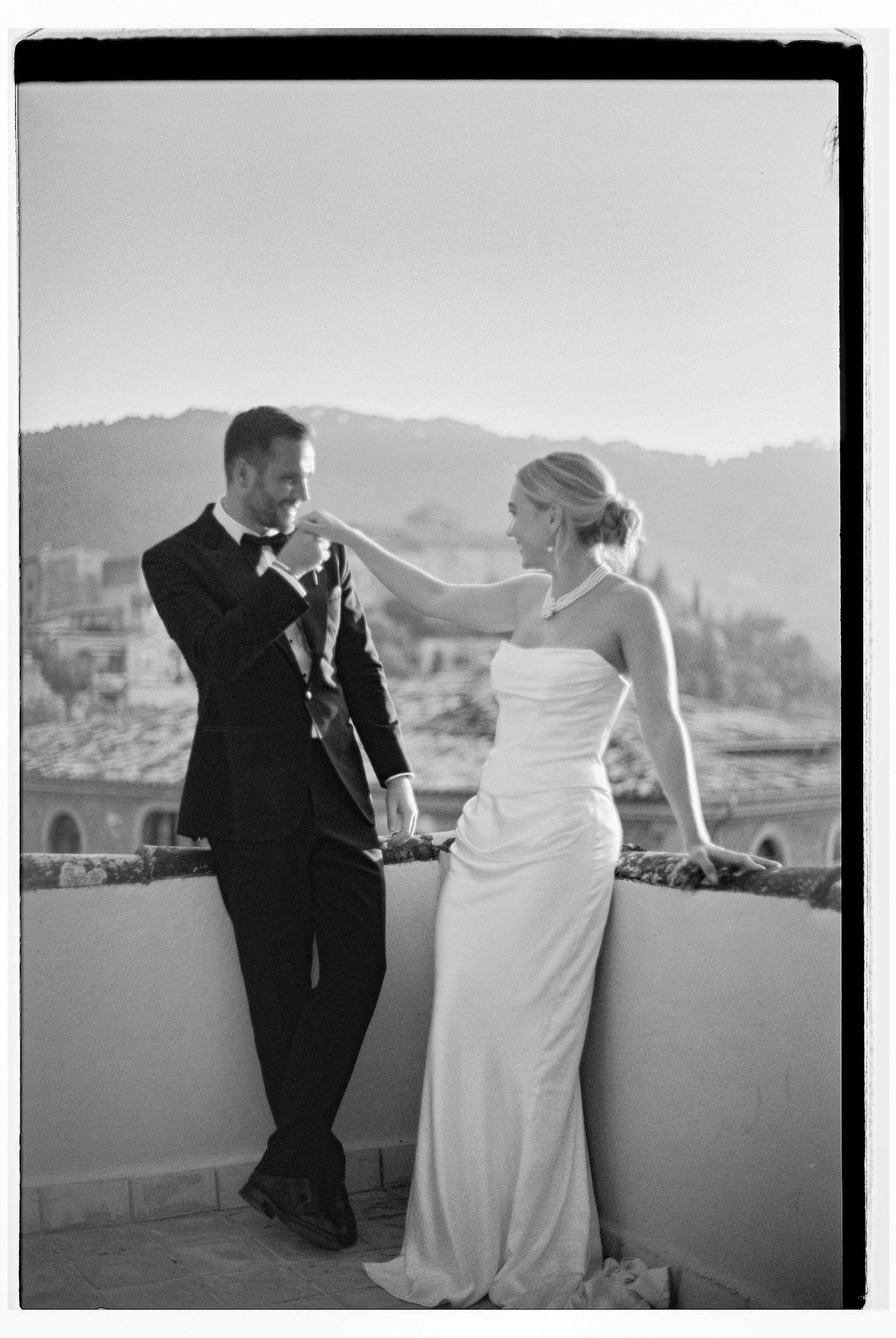 A couple in wedding attire posing playfully against a mountain backdrop at sunset.
