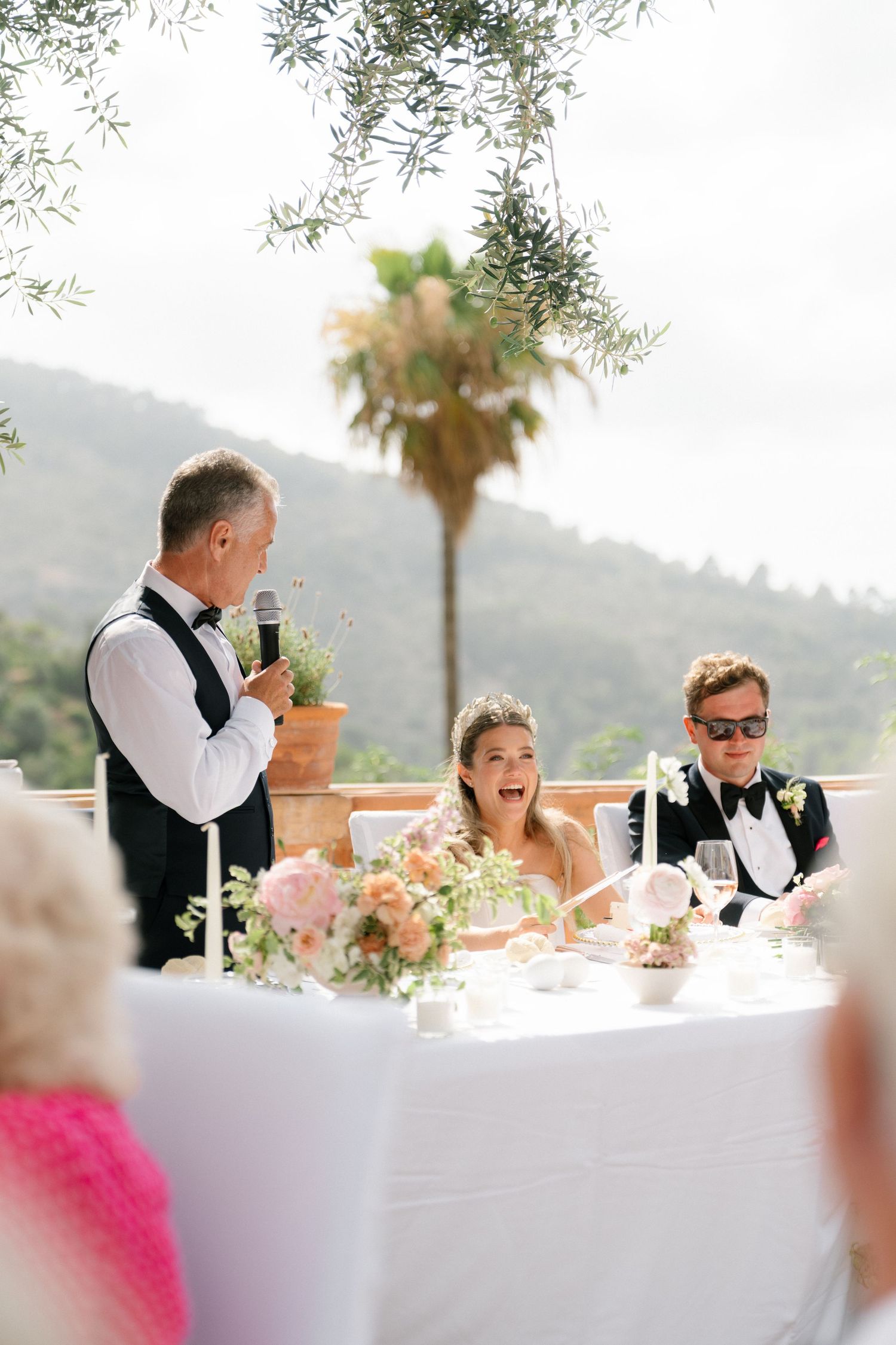 Wedding reception speech at an outdoor venue with mountain views and palm trees.