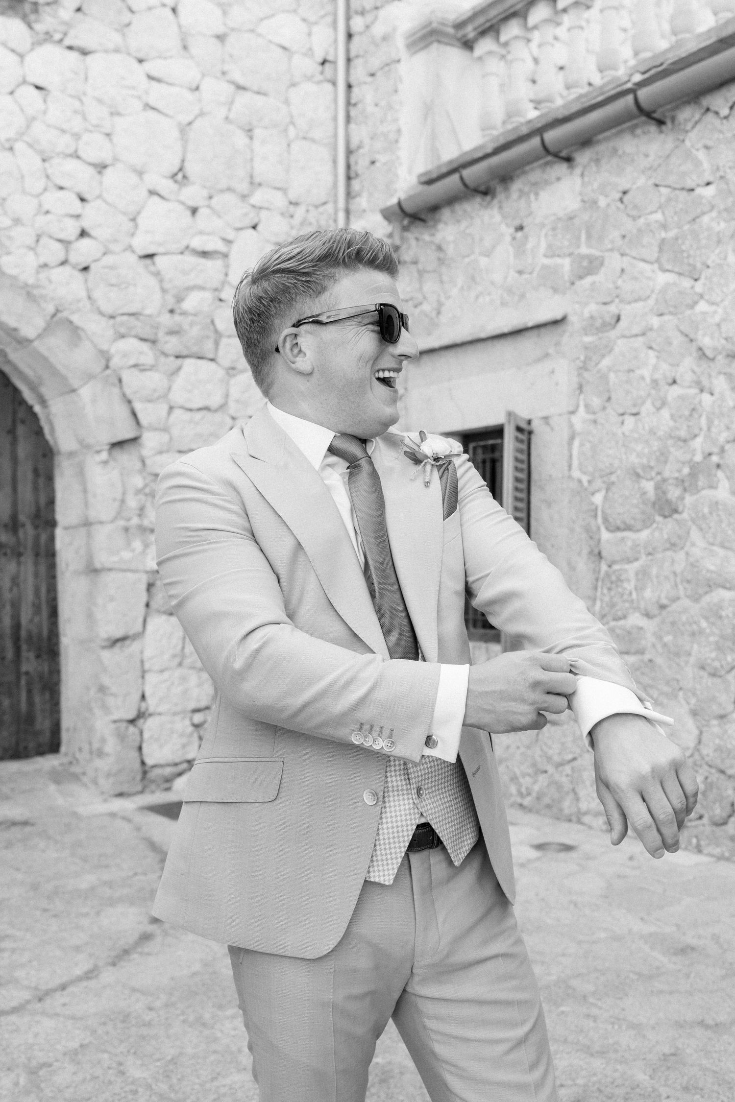 Candid moments of groomsmen in light suits laughing and posing by stone walls.